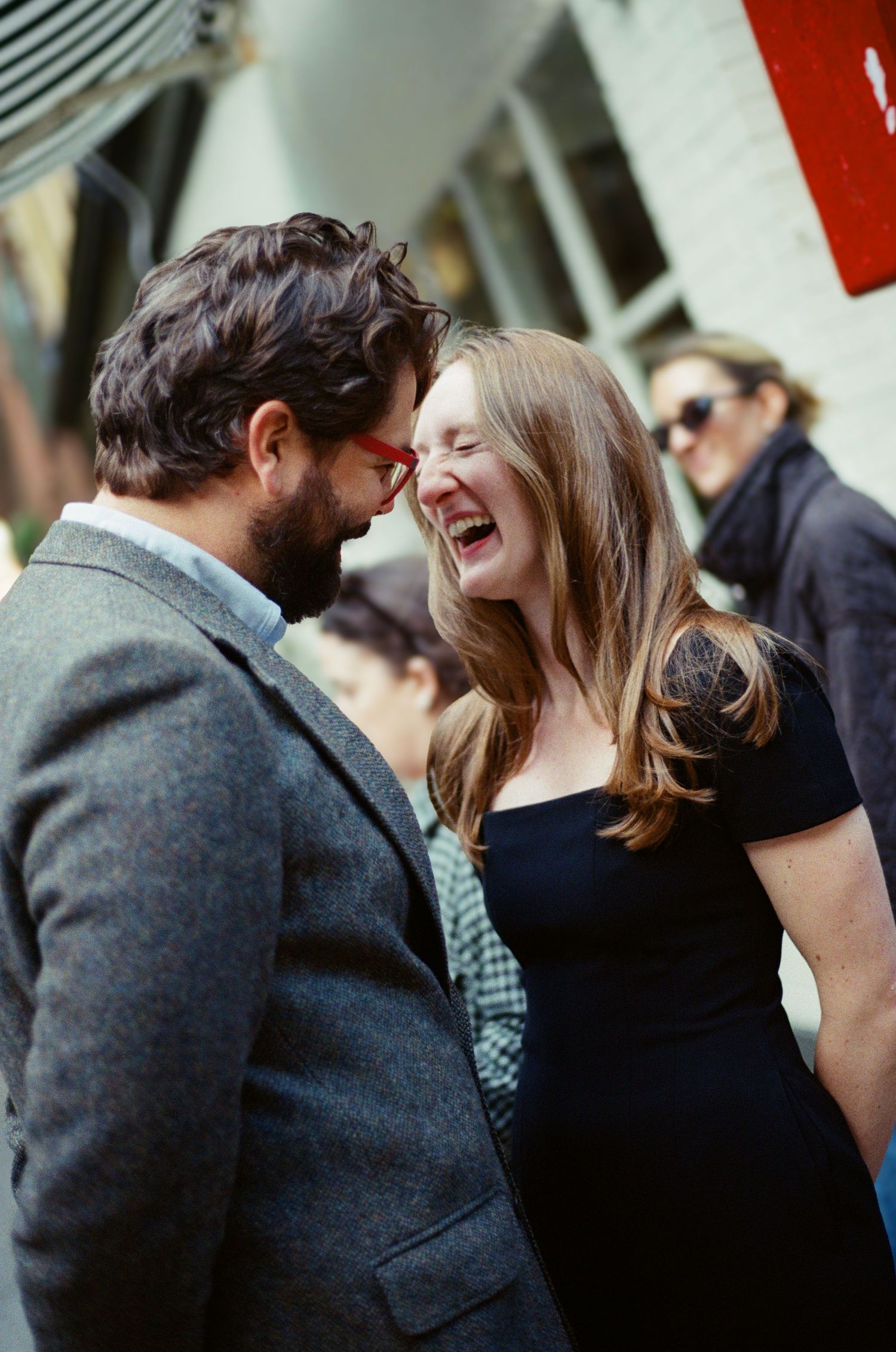 A couple shares an intimate moment of laughter while standing close together outdoors.