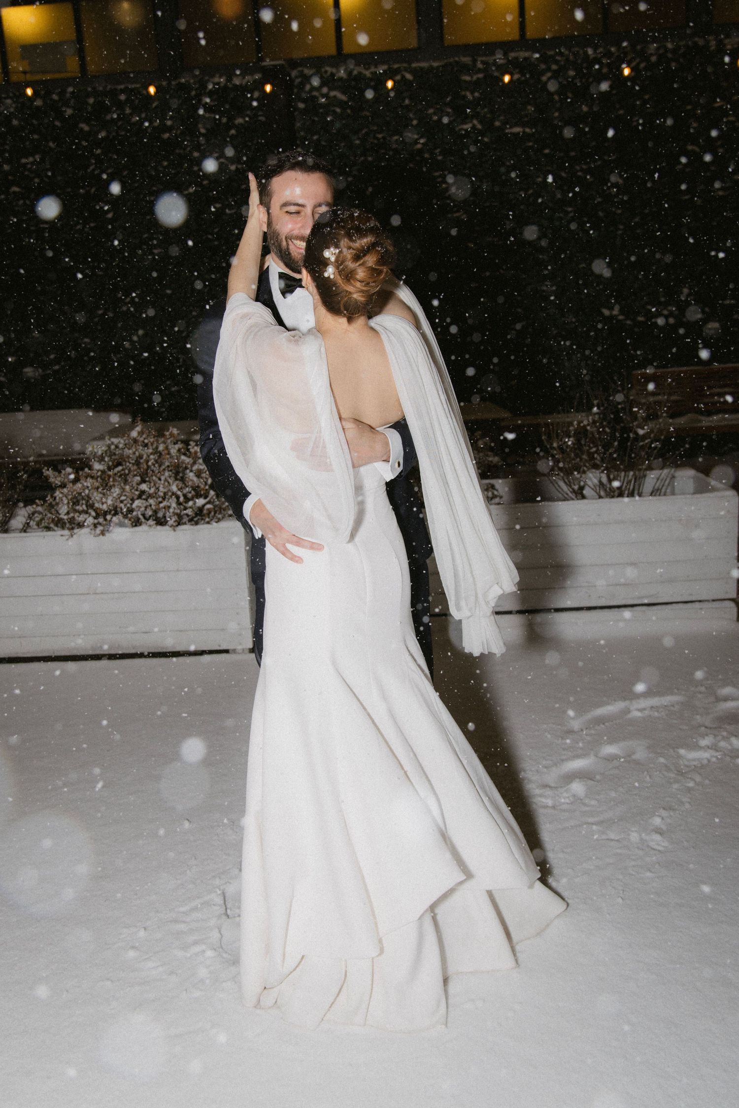 Newlyweds share a romantic dance outside in falling snow.