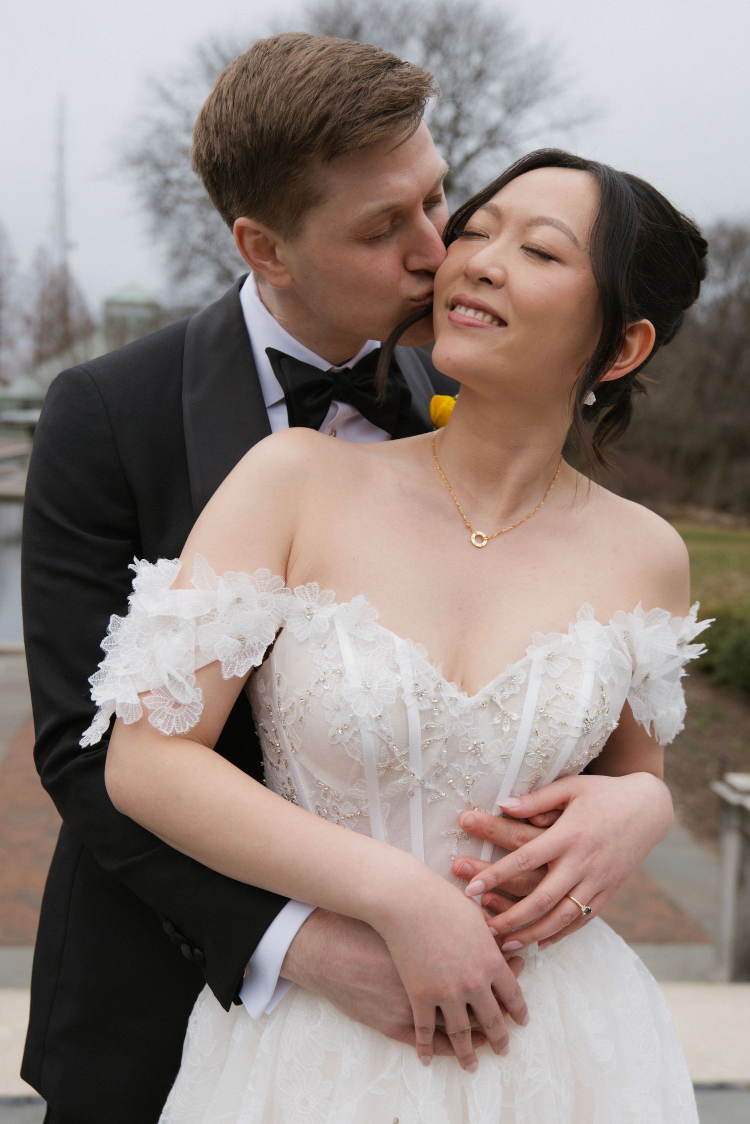 Romantic newlywed couple embraces intimately in formal wedding attire during outdoor photo session.