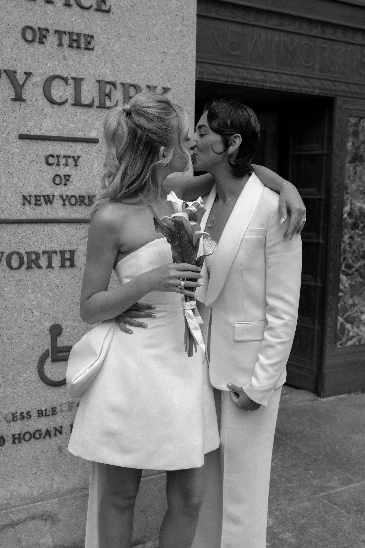 A couple in white outfits share a romantic moment outside the City Clerk's office in New York City.