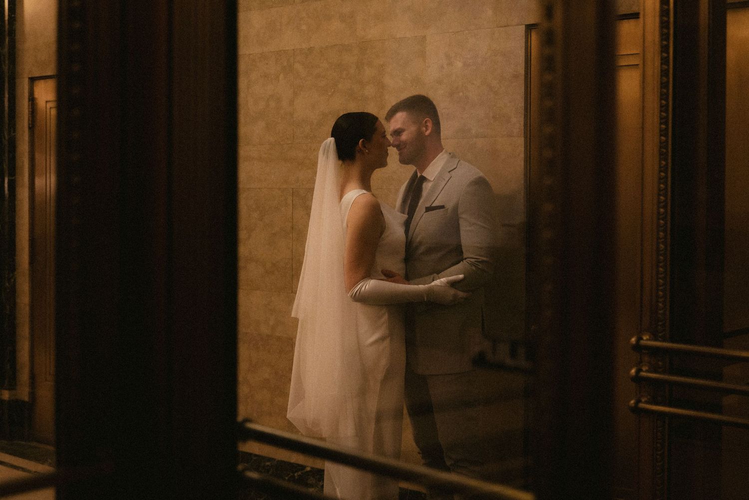 Bride and groom share an intimate moment in a warmly lit elegant venue, bride in white gown with veil.