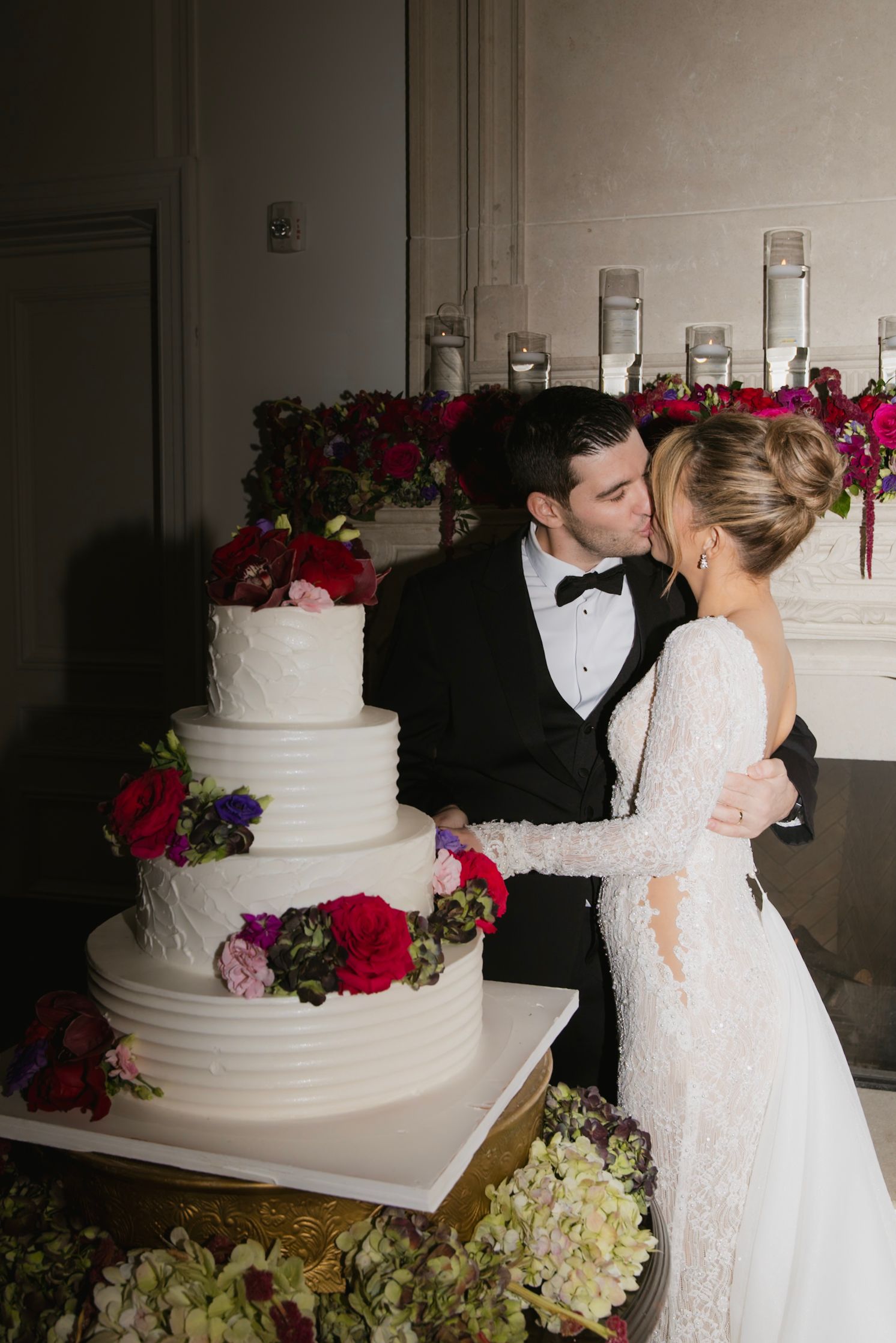 Elegant white tiered wedding cake decorated with vibrant red and pink flowers.