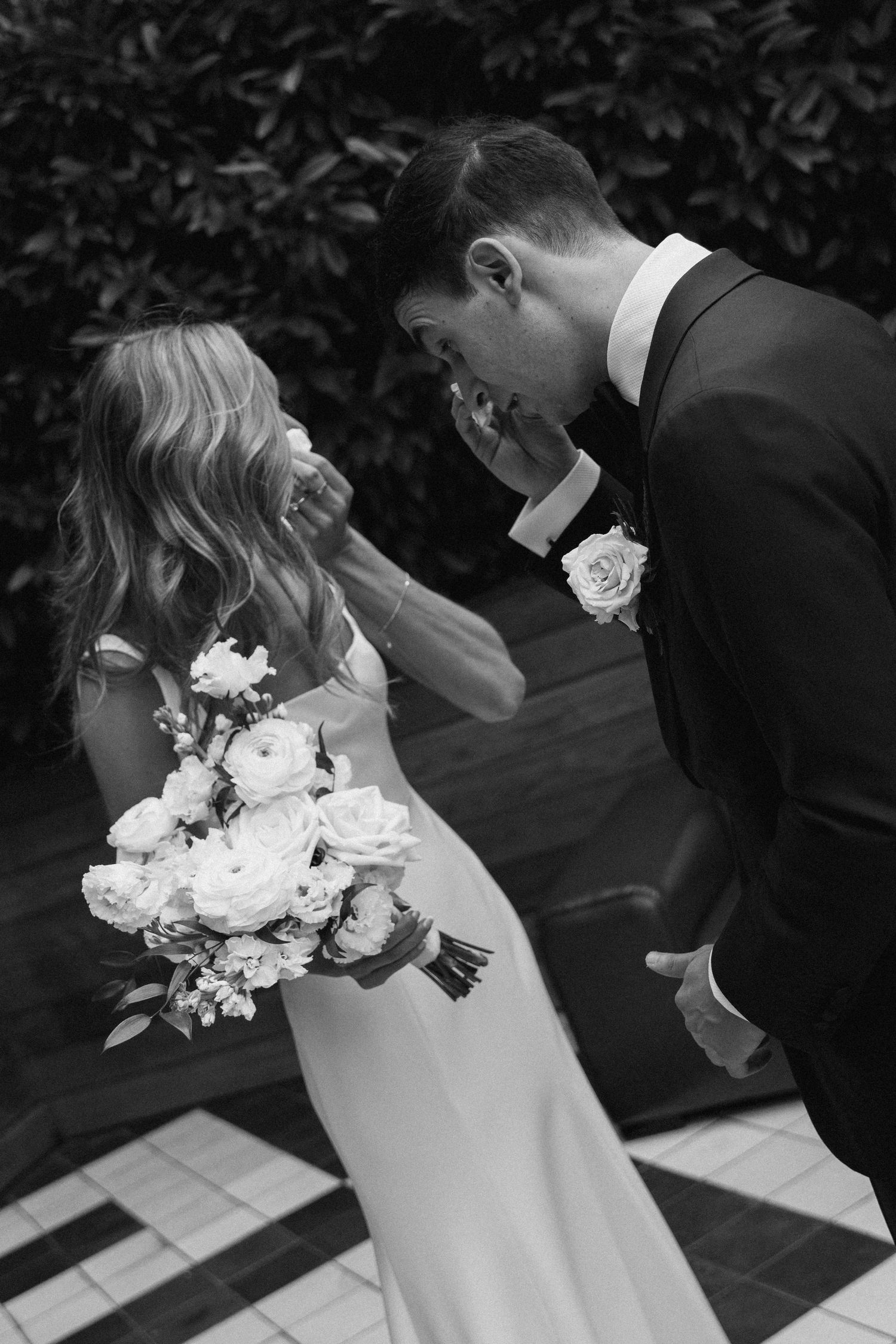 A romantic black and white sequence of a couple sharing a kiss while holding a white floral bouquet.