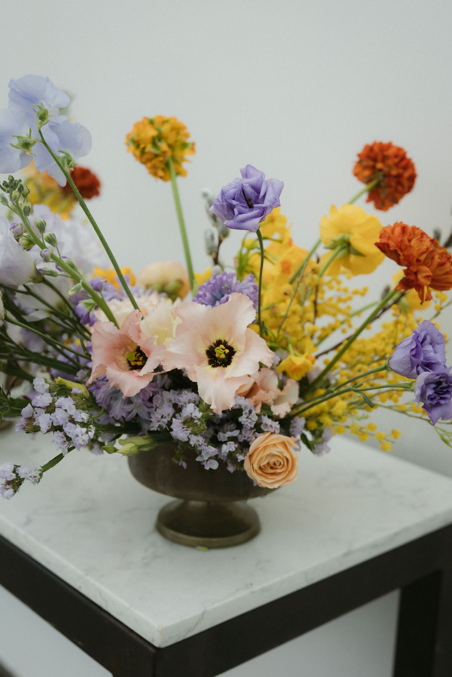 Colorful wedding floral arrangement featuring mixed seasonal blooms in antique brass pedestal vase.