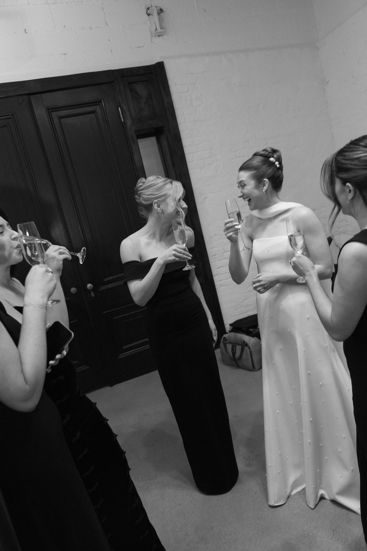 Wedding party shares pre-ceremony drinks and laughter in a casual black and white moment.