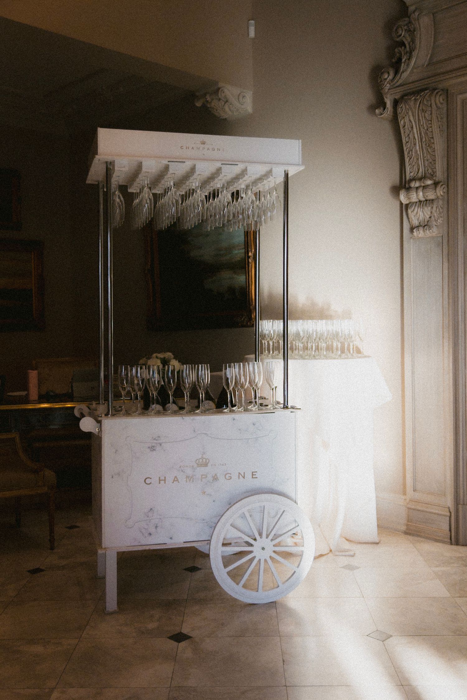 Vintage-style white champagne cart with glass holders and decorative wheels in elegant room.