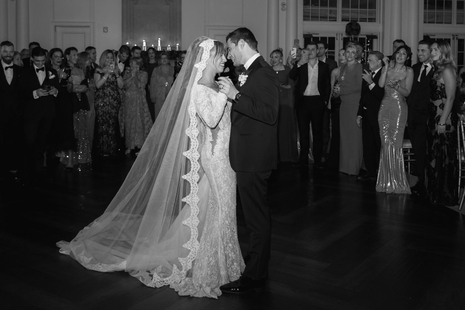 Couple performs their first dance at an elegant wedding reception while guests watch in formal attire.