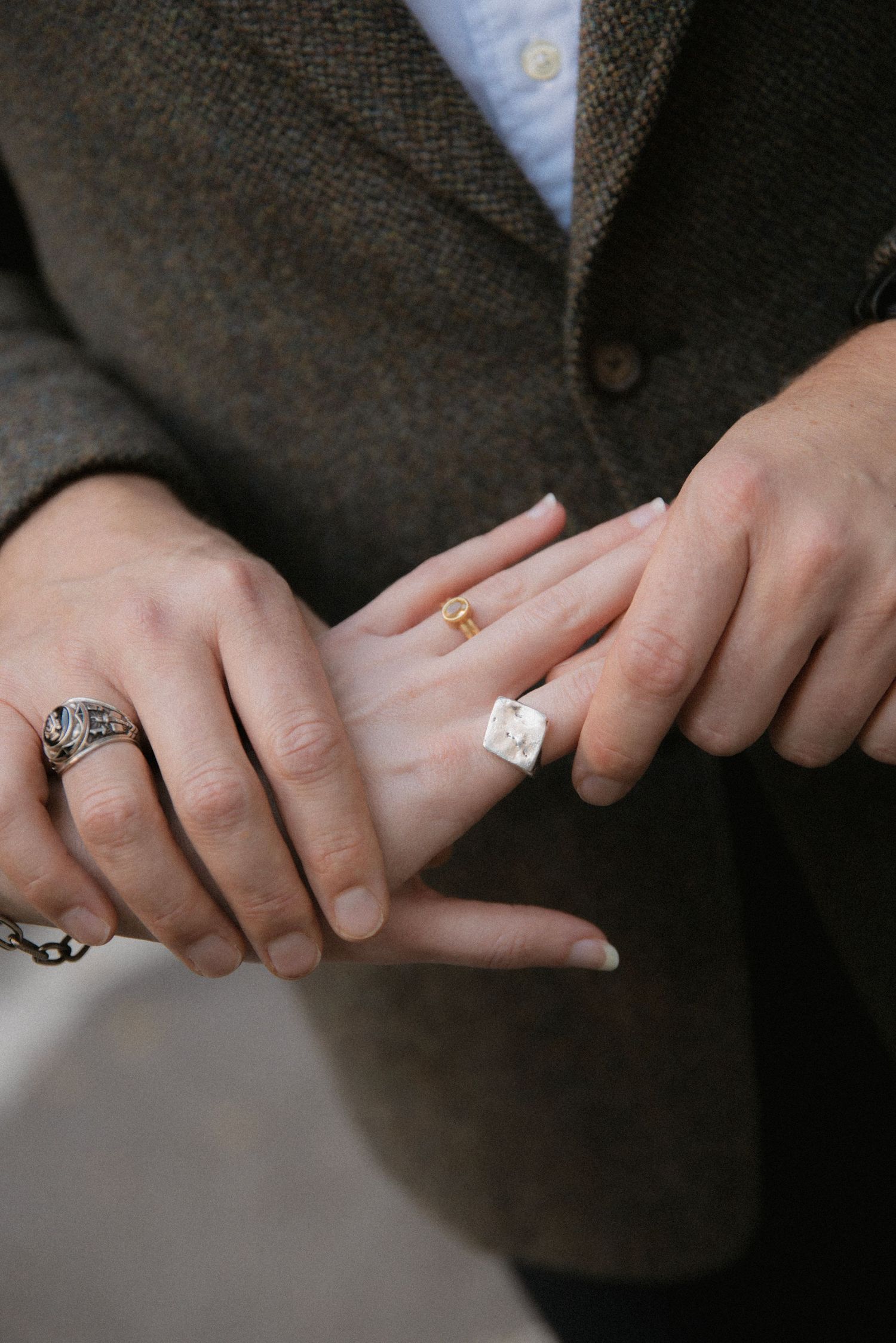 Close-up shot of hands wearing elegant wedding rings and engagement rings against a dark suit jacket background.