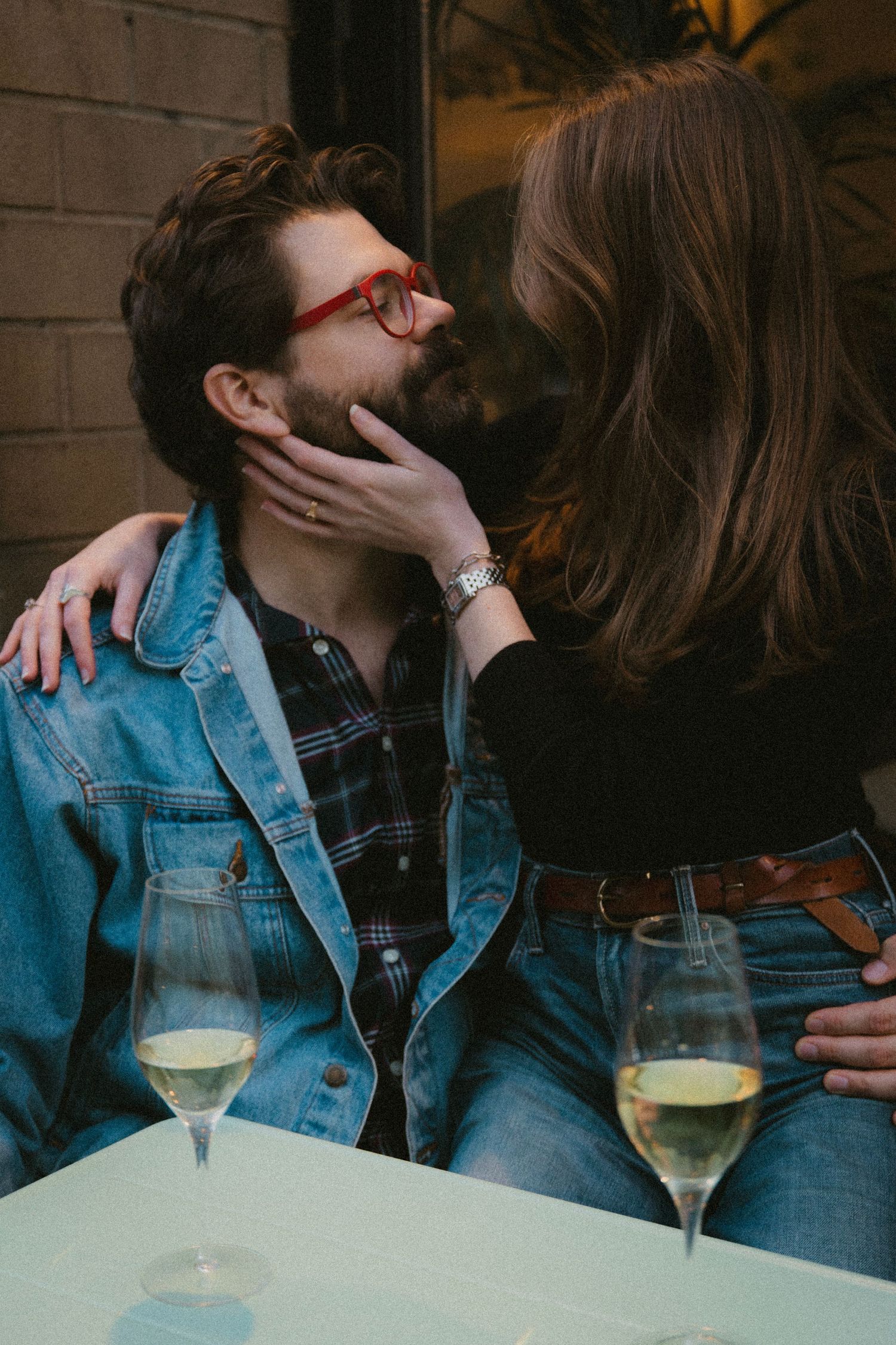 A couple in denim sharing intimate moments at a wine bar with glasses of white wine on the table.
