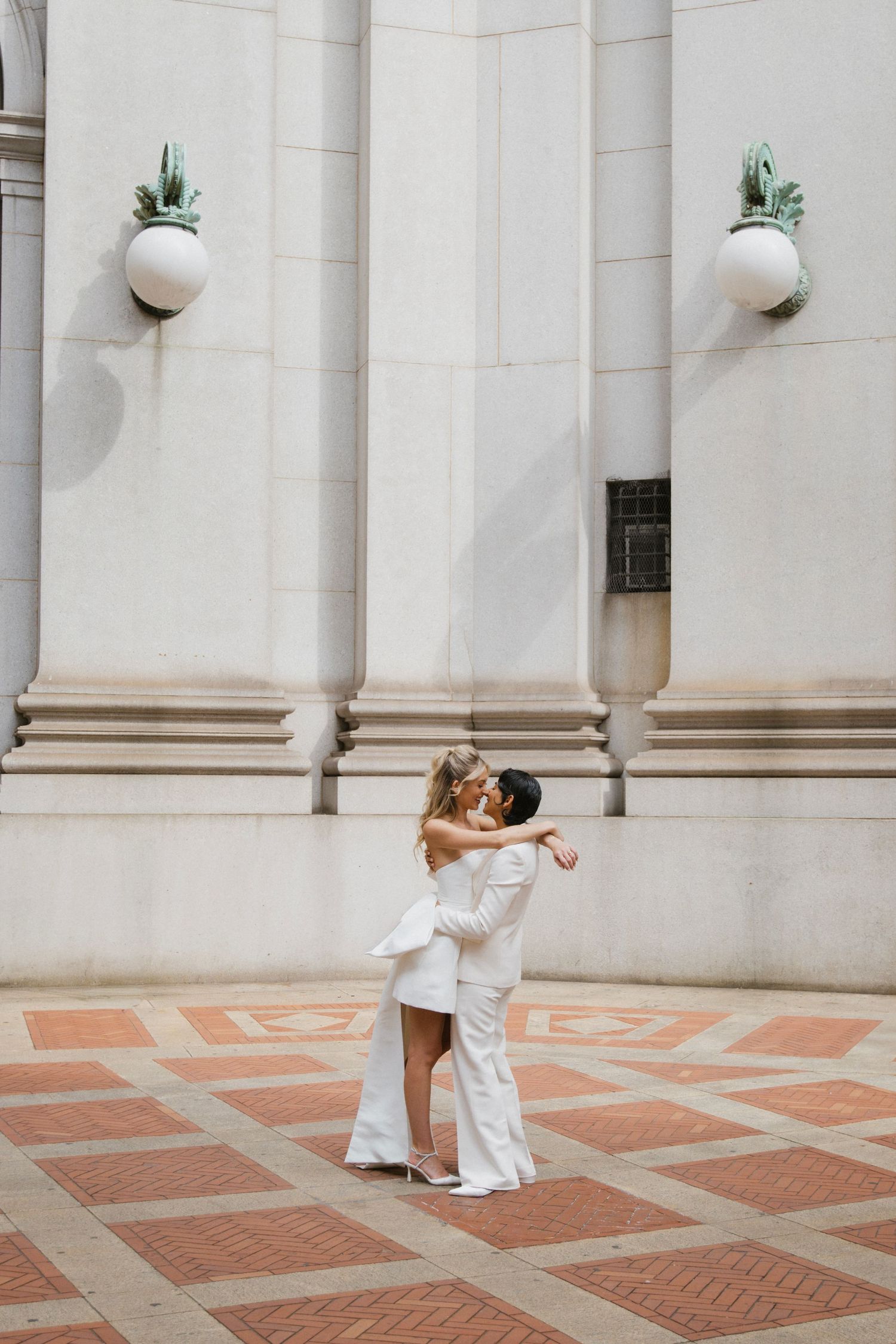 A couple in white outfits dancing together in front of a columned building.