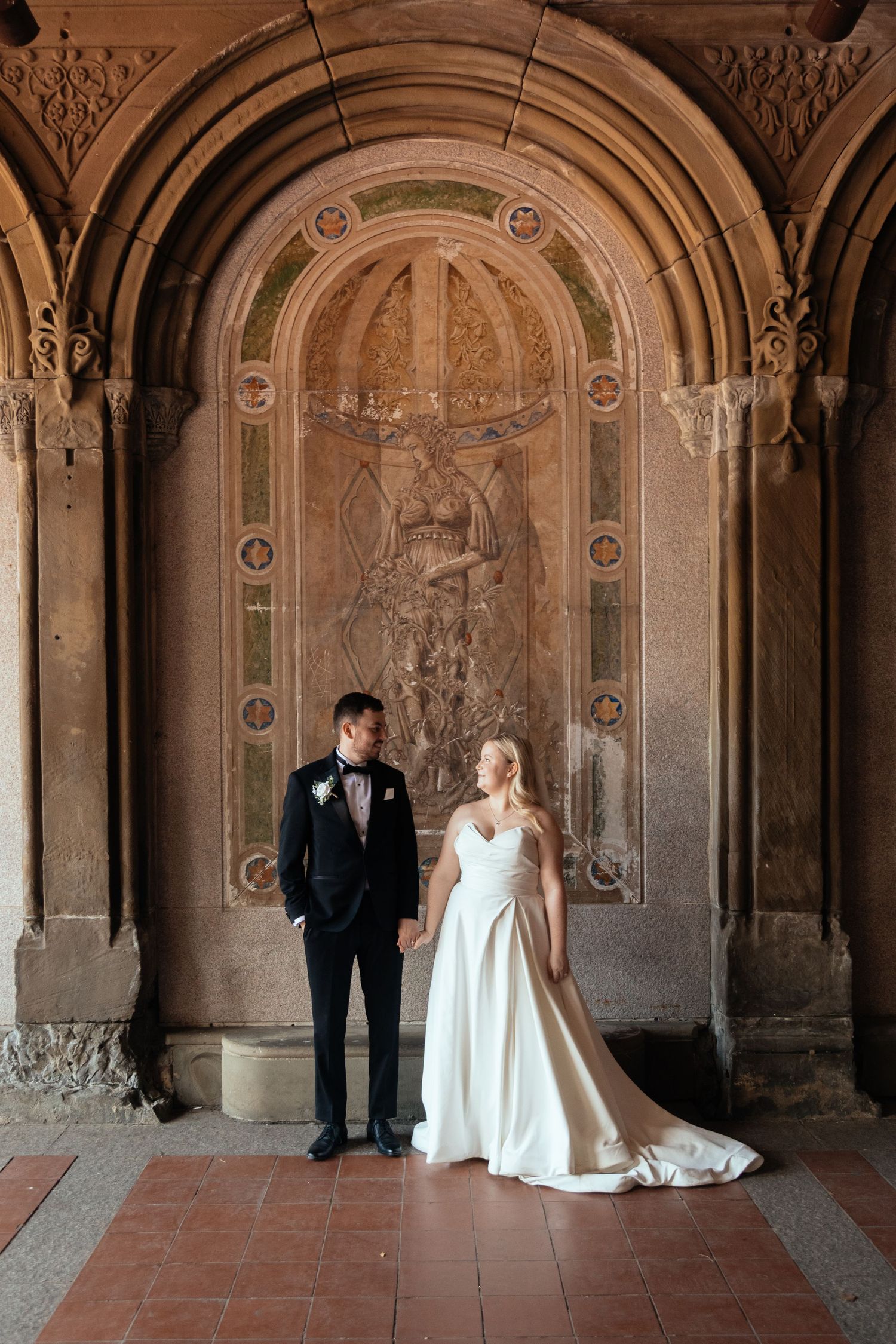 A wedding couple poses in four similar shots under ornate stone arches at historic Bethesda Terrace in Central Park.