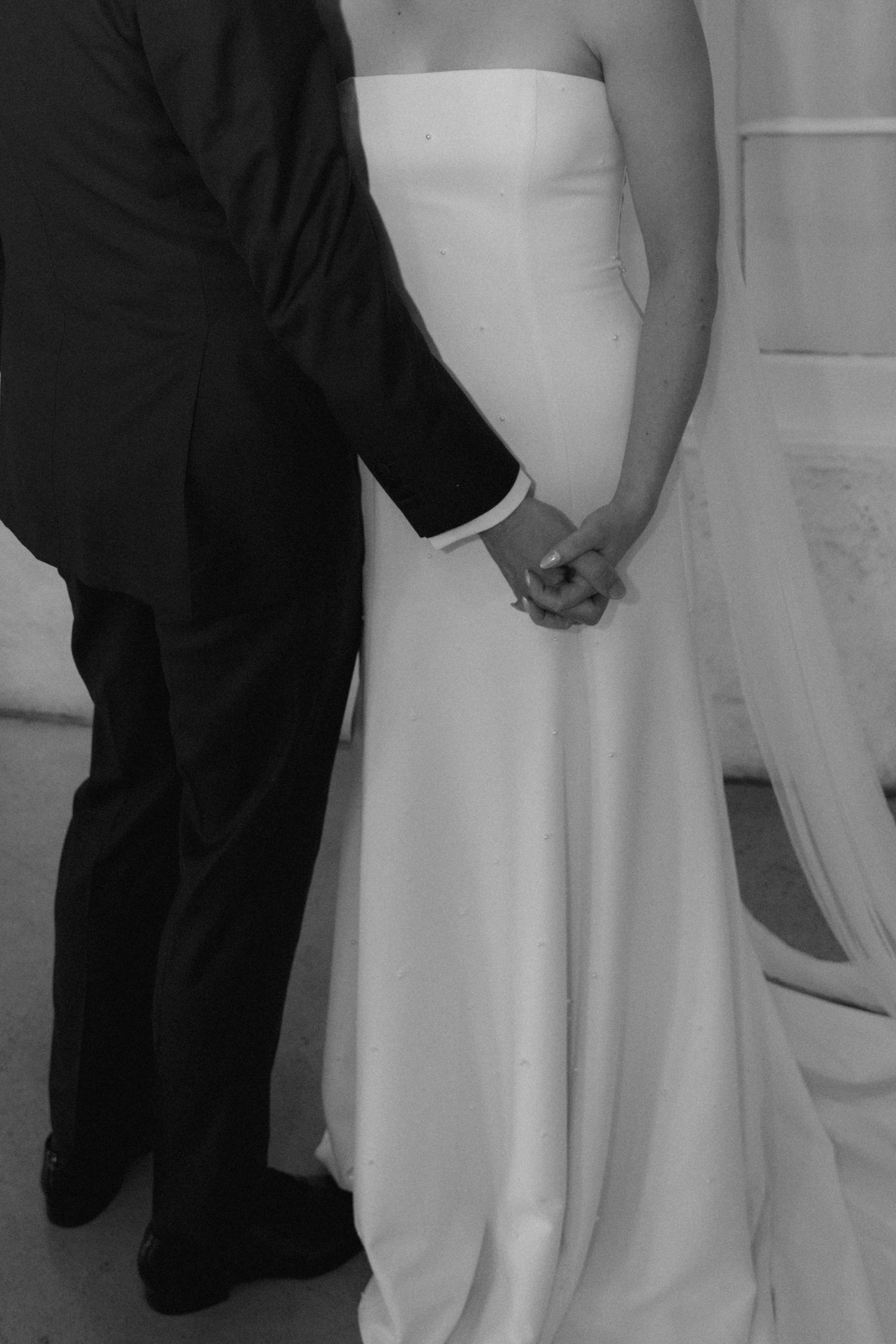 Black and white photo showing the lower half of two people holding hands during a wedding ceremony.
