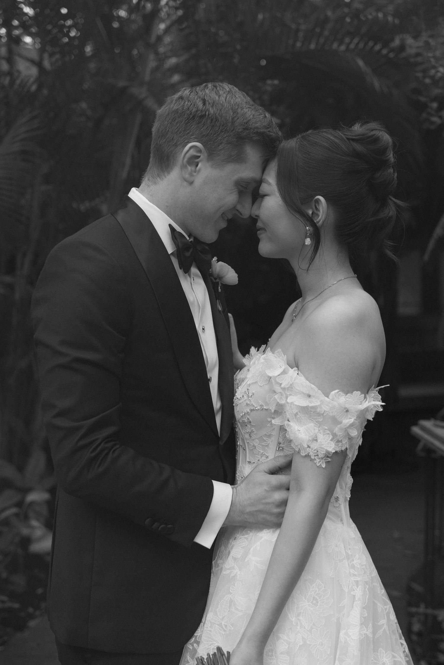 A romantic black and white wedding photo shows a tender moment between newlyweds in formal attire.