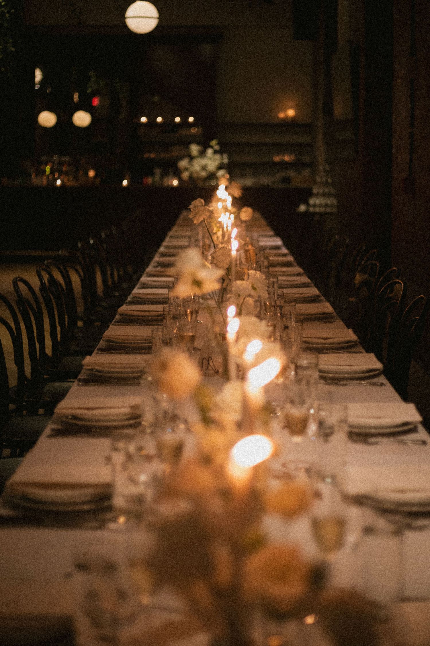 An elegant wedding reception table setting with glowing candles and white linens in a dimly lit room.