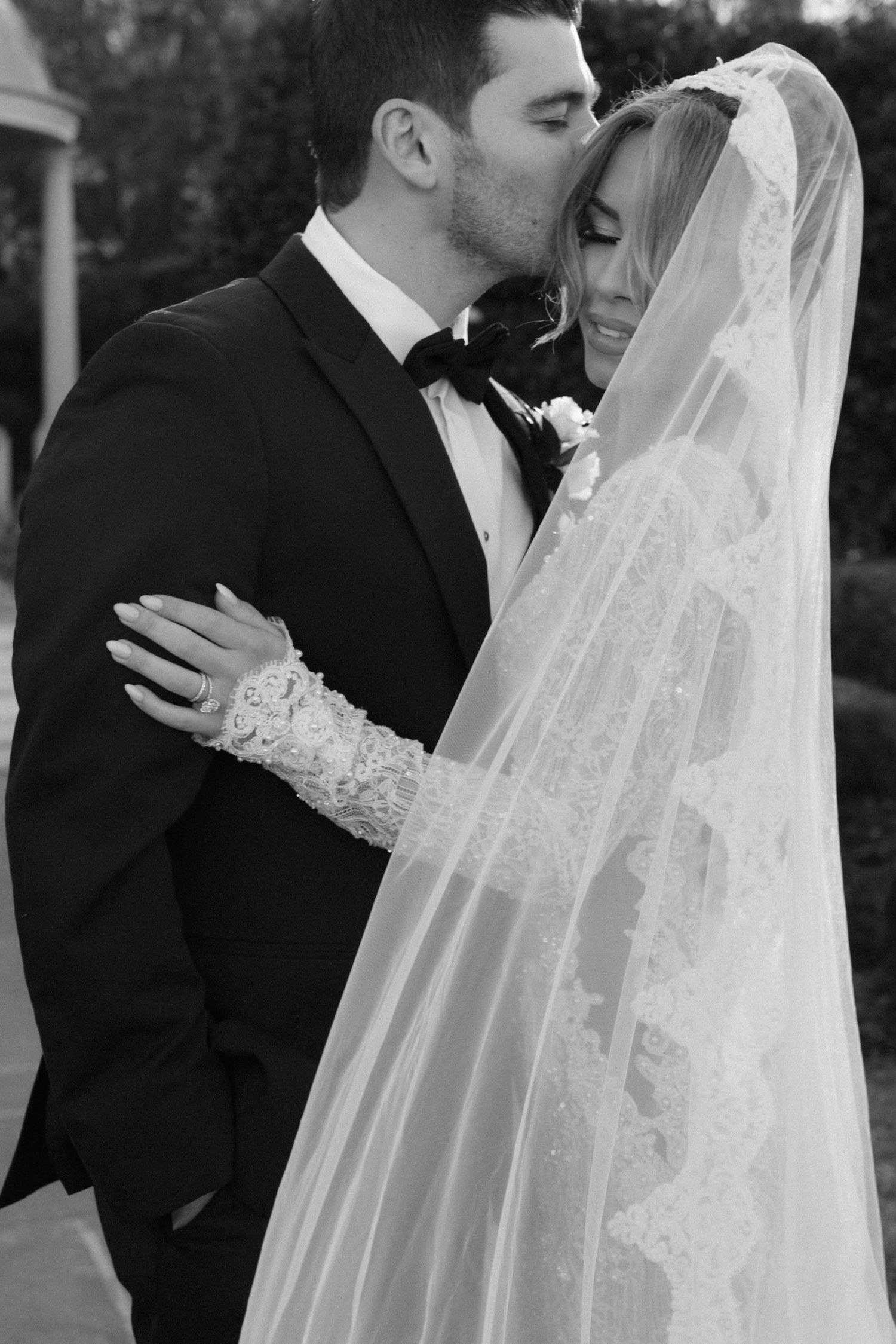 Black and white wedding portrait series showing intimate moments between bride in lace veil and groom in tuxedo.