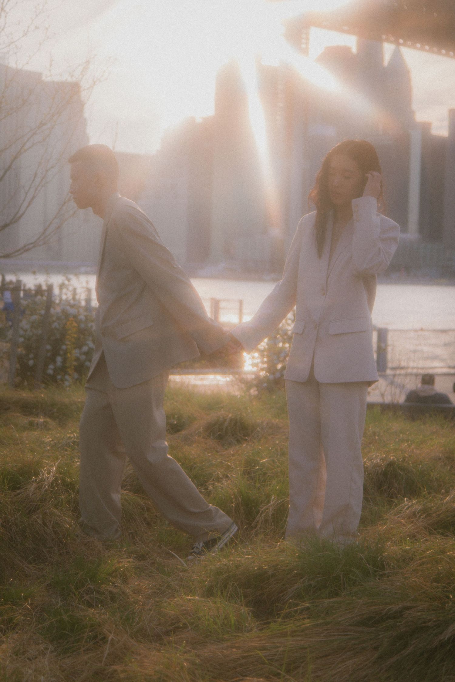 Two people embracing in a sunlit field with tall grass at sunset creating a dreamy, romantic atmosphere.