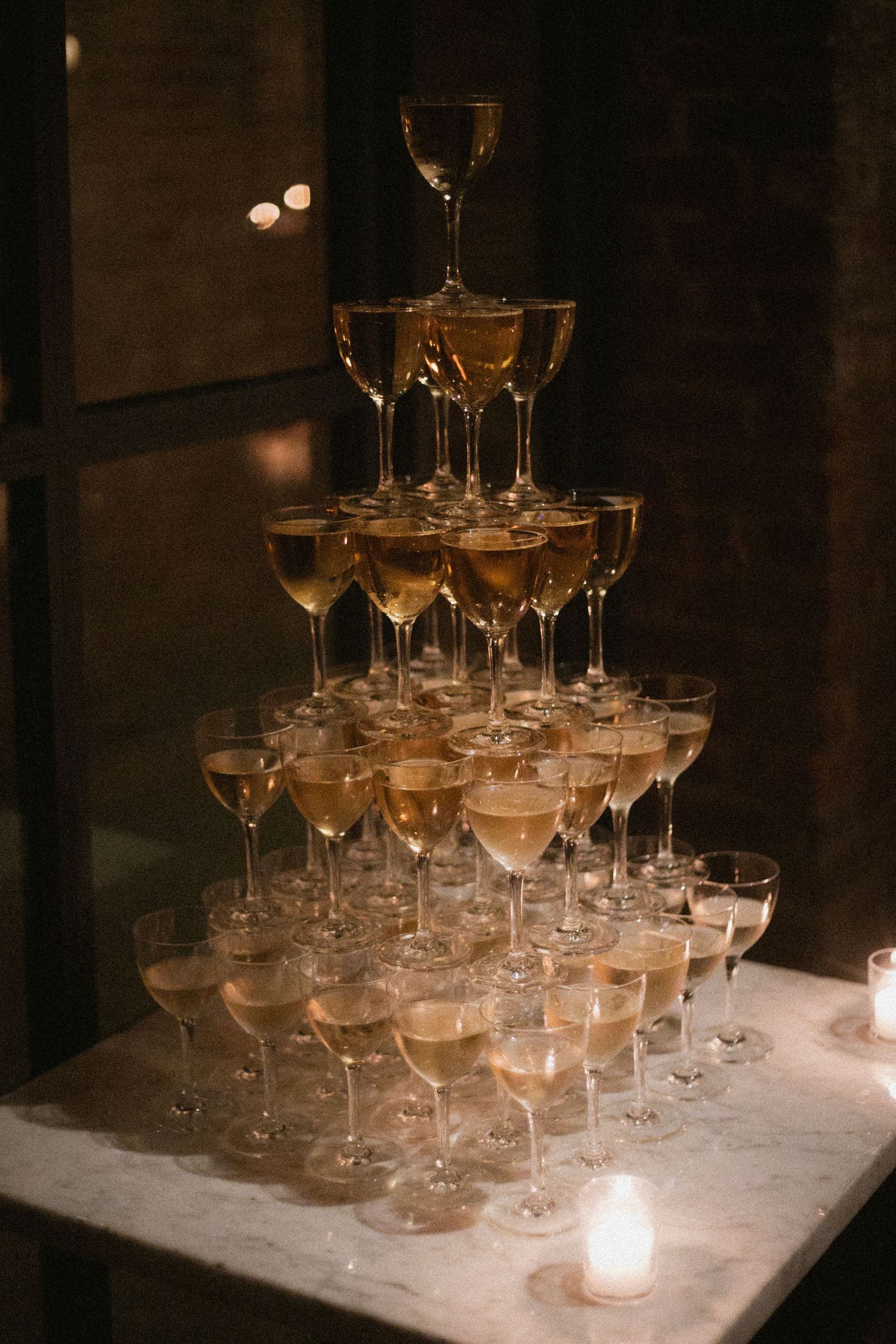 Elegant champagne glasses arranged in a pyramid formation on a white surface with soft candlelight illumination.