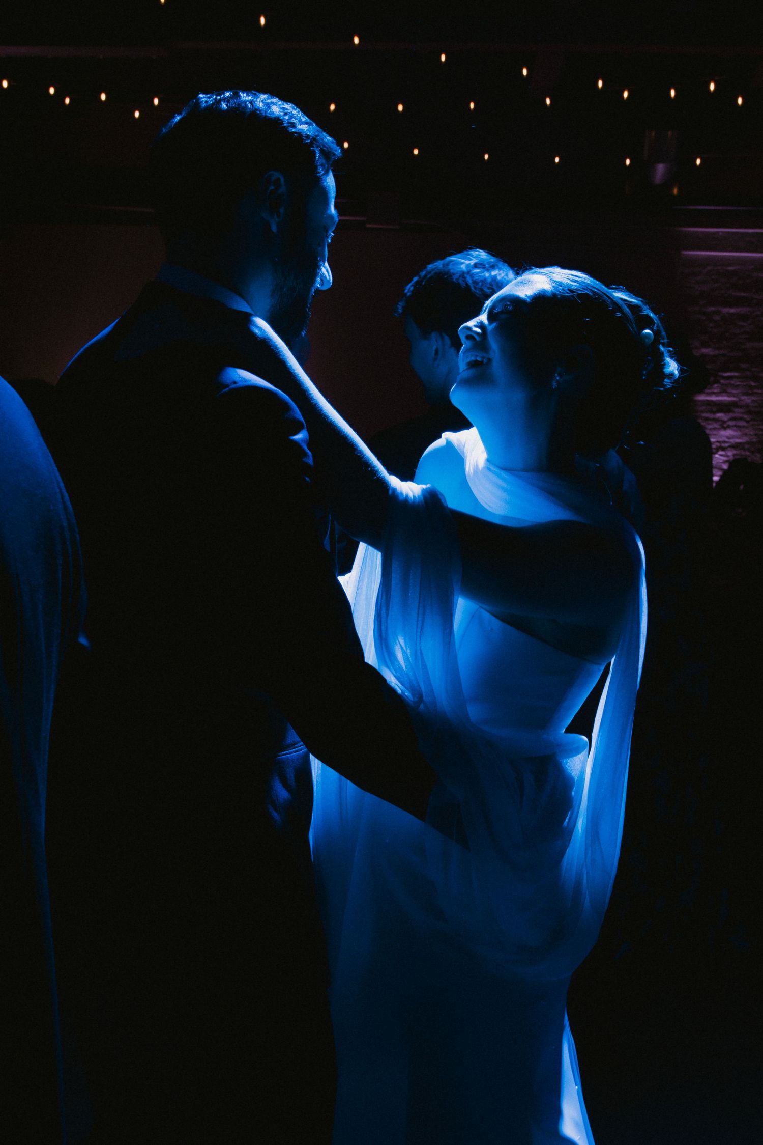 A romantic dance moment captured in dramatic blue lighting at a wedding reception.