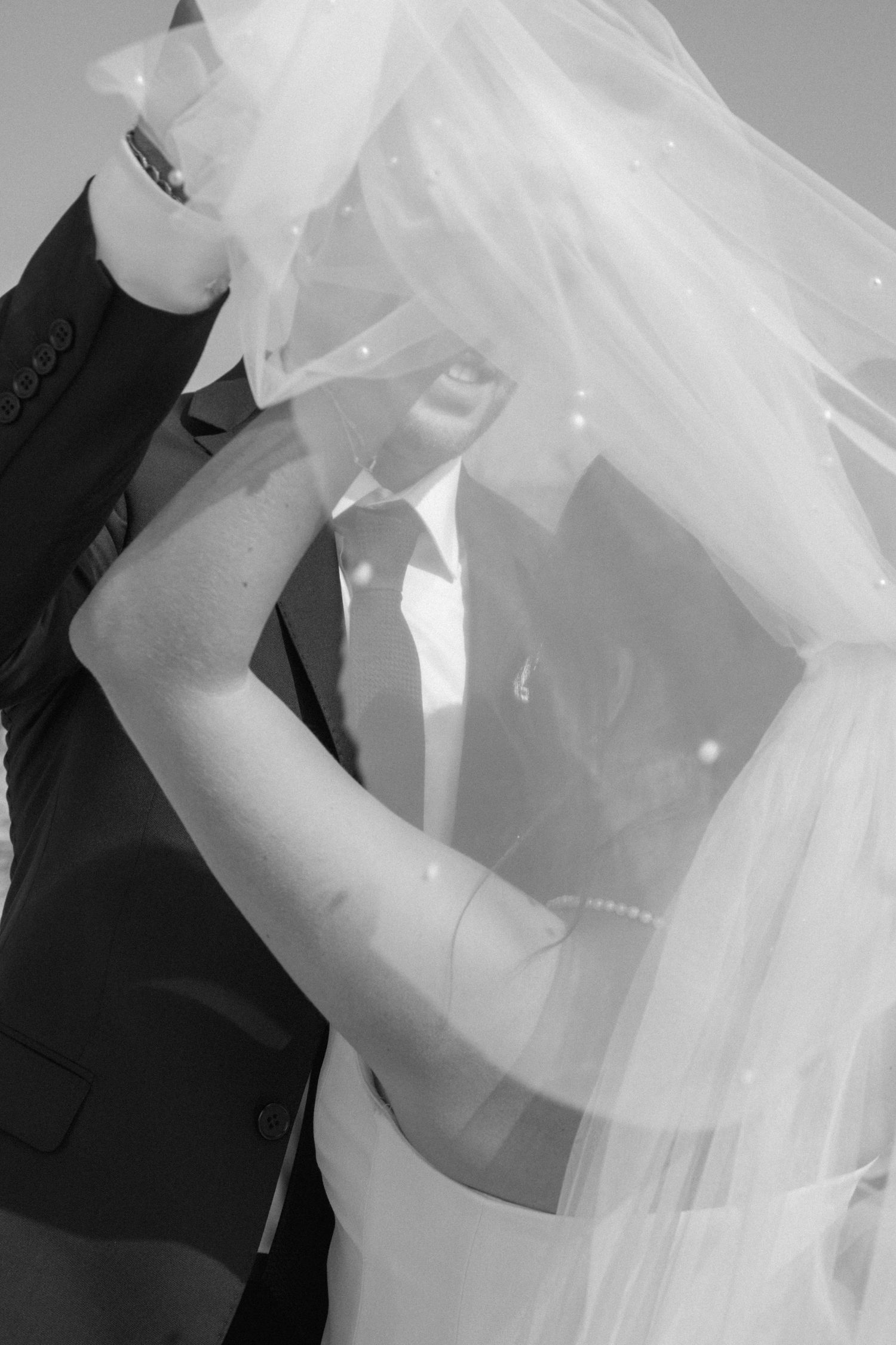 A black and white wedding photograph showing a romantic moment through a delicate veil.