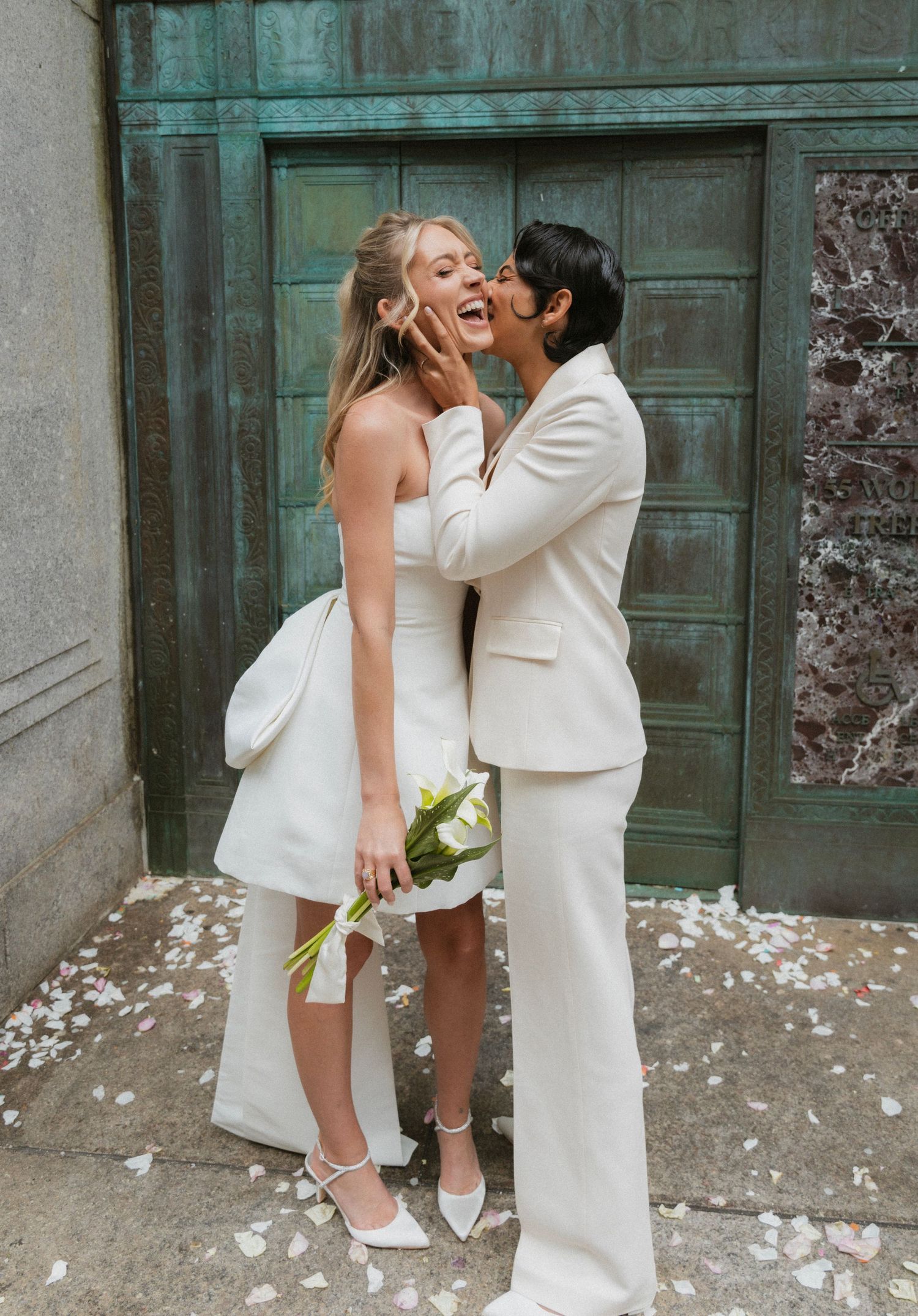 A romantic wedding scene with two people in white outfits embracing against a turquoise door.