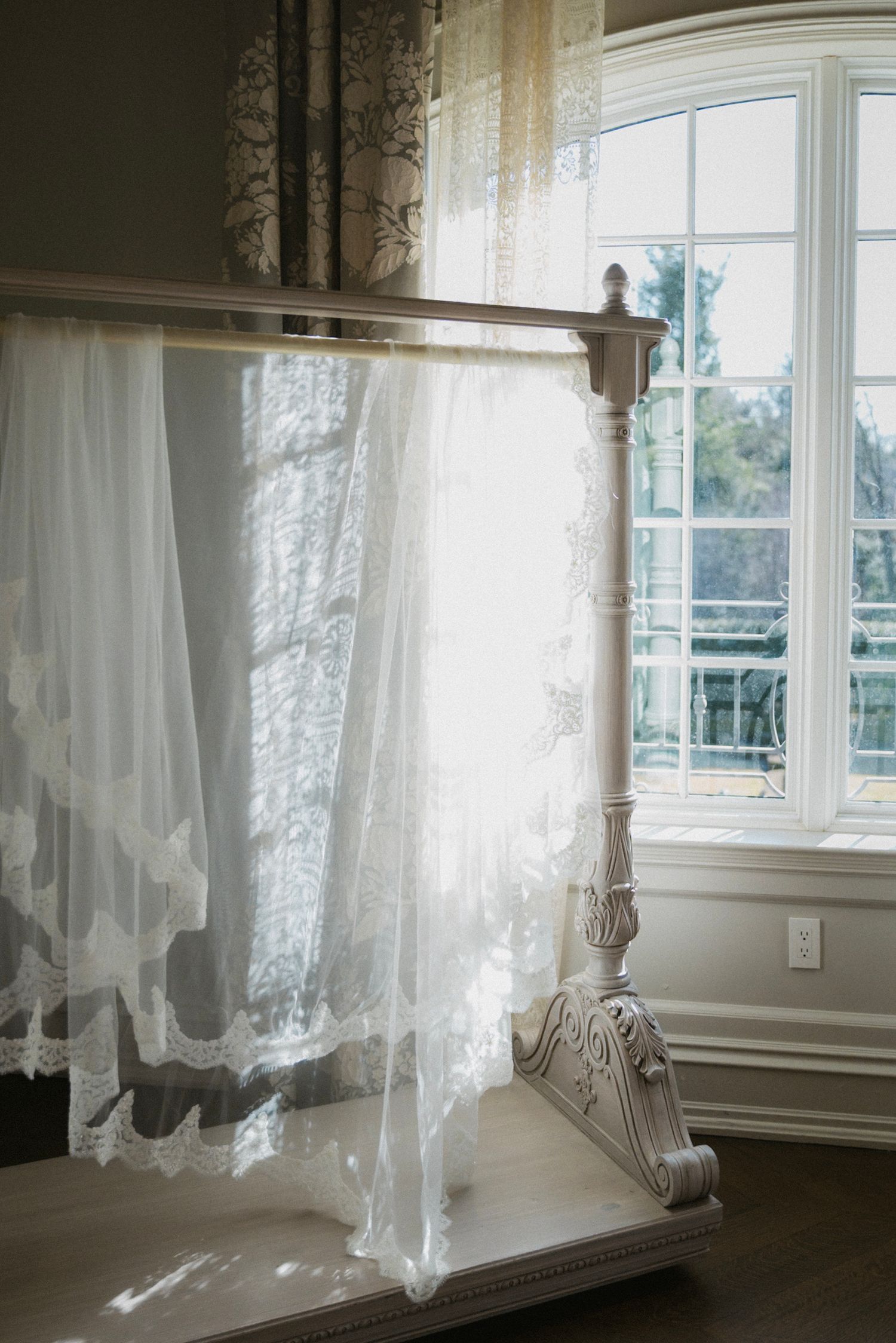 Flowing white wedding veil draped on an ornate display stand near a sunlit window.