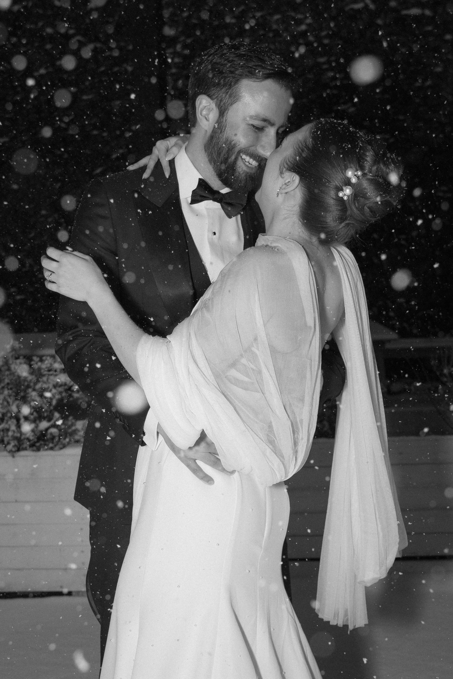 A couple shares an intimate dance at a wedding reception with snowy effects overlaid in black and white.