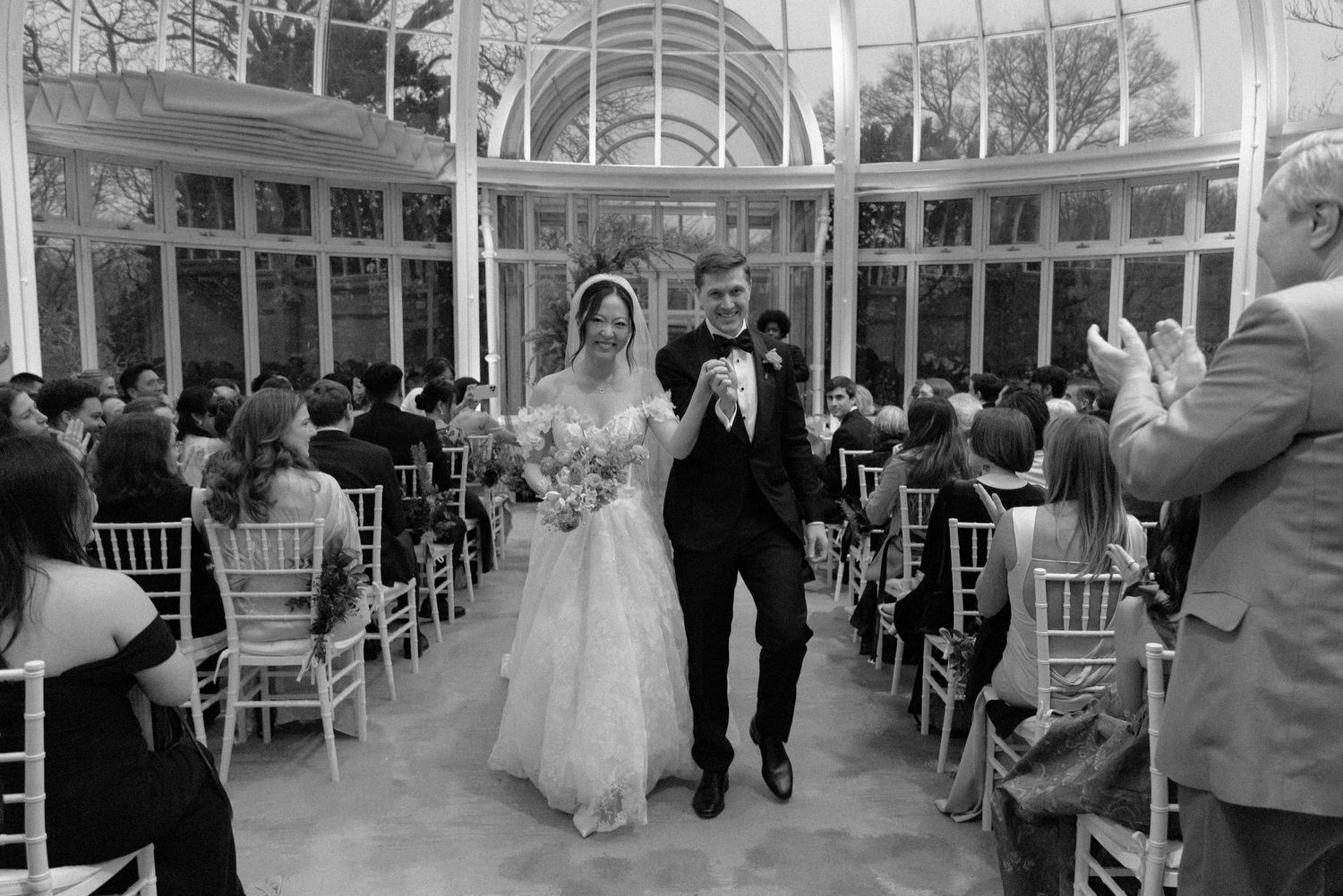 Black and white panorama of a wedding ceremony in a grand glass-ceiling venue.