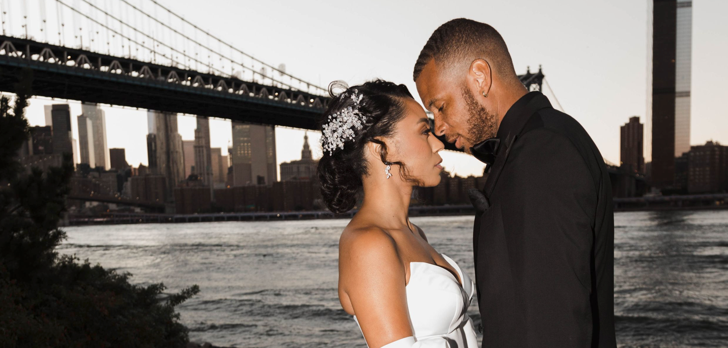 A romantic couple embraces in silhouette against a cityscape with multiple bridges visible at sunset.