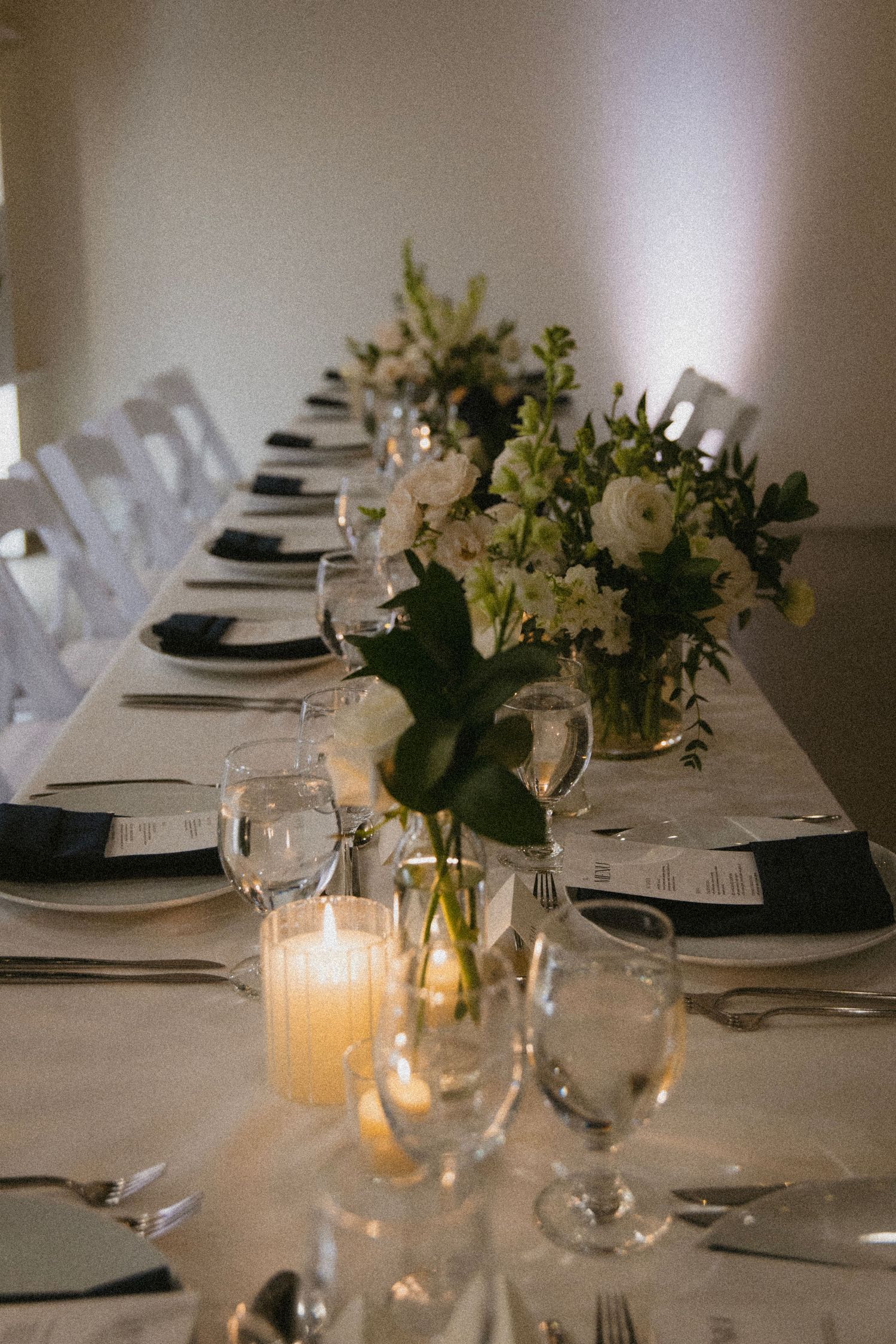 An elegant wedding table setting with white floral centerpieces, candles and formal place settings.