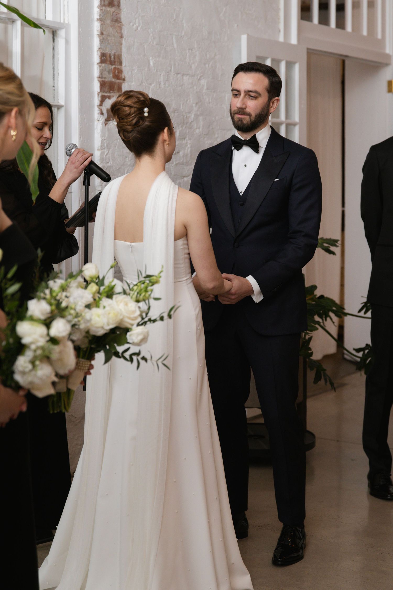 An elegant wedding ceremony moment with beautiful white floral arrangements against brick walls.