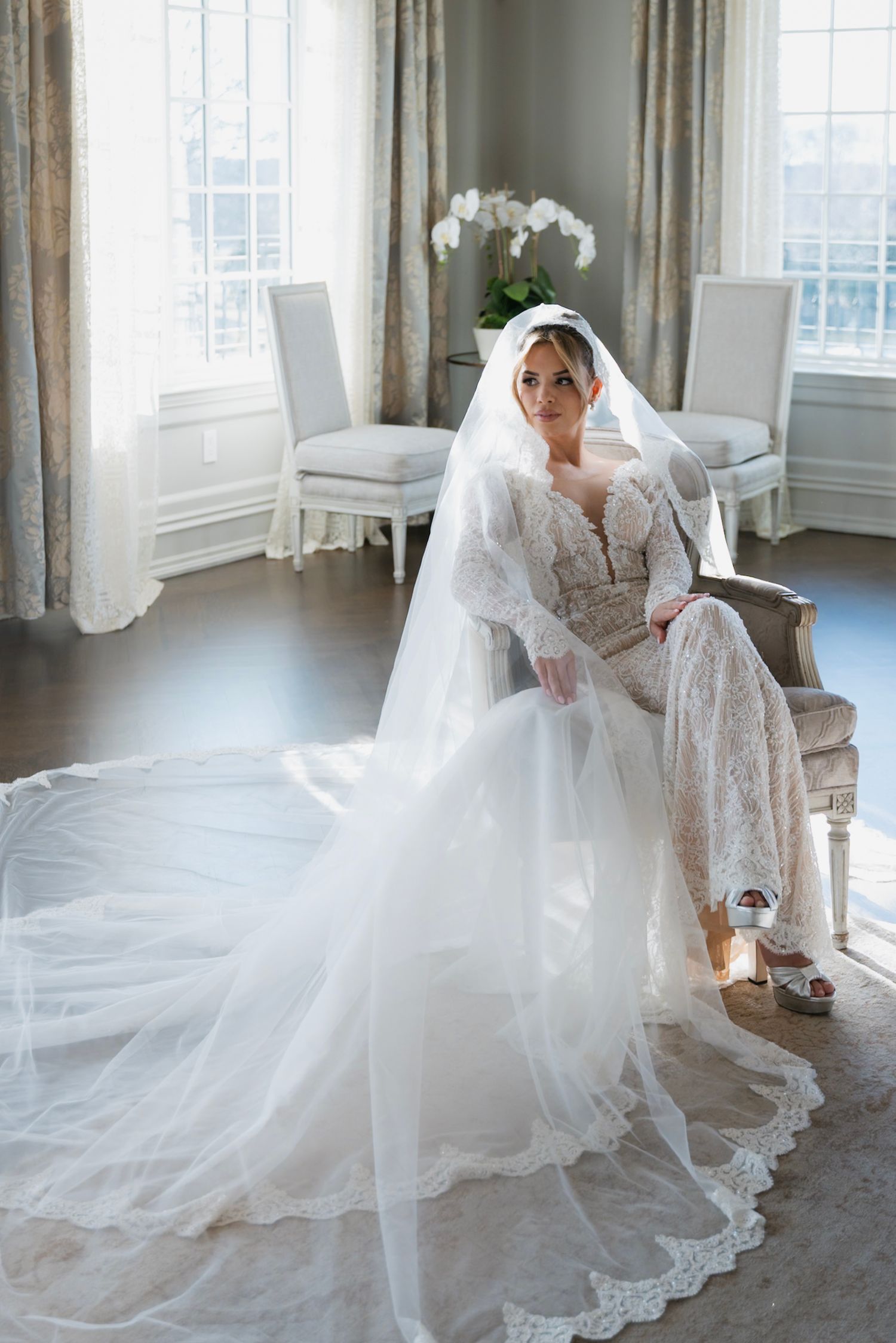 An elegant bridal gown with lace details and flowing train photographed in a bright sunlit room.