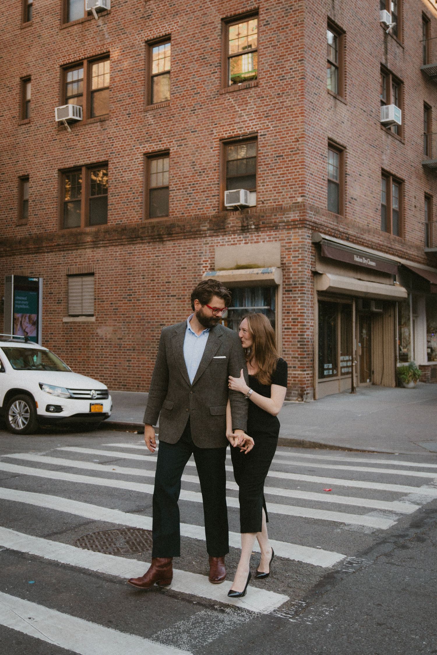 A couple poses playfully on a crosswalk near brick apartment buildings in an urban setting.