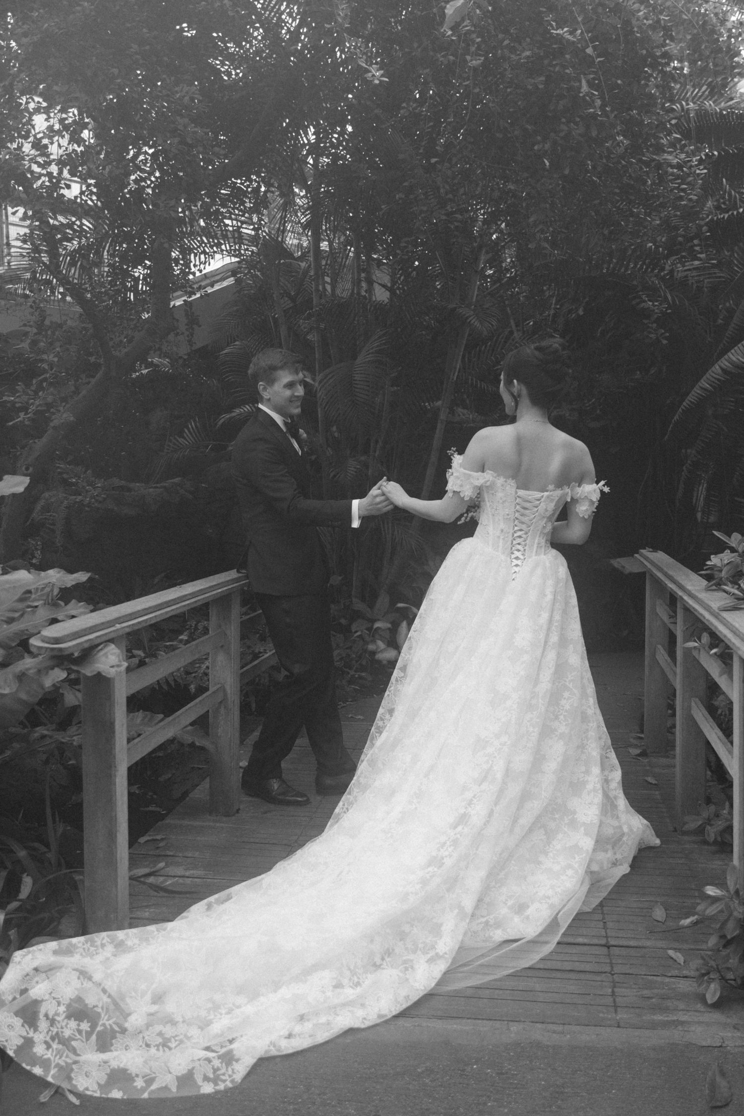 A series of black and white photographs capturing the flowing train of a lace wedding dress on a wooden walkway.