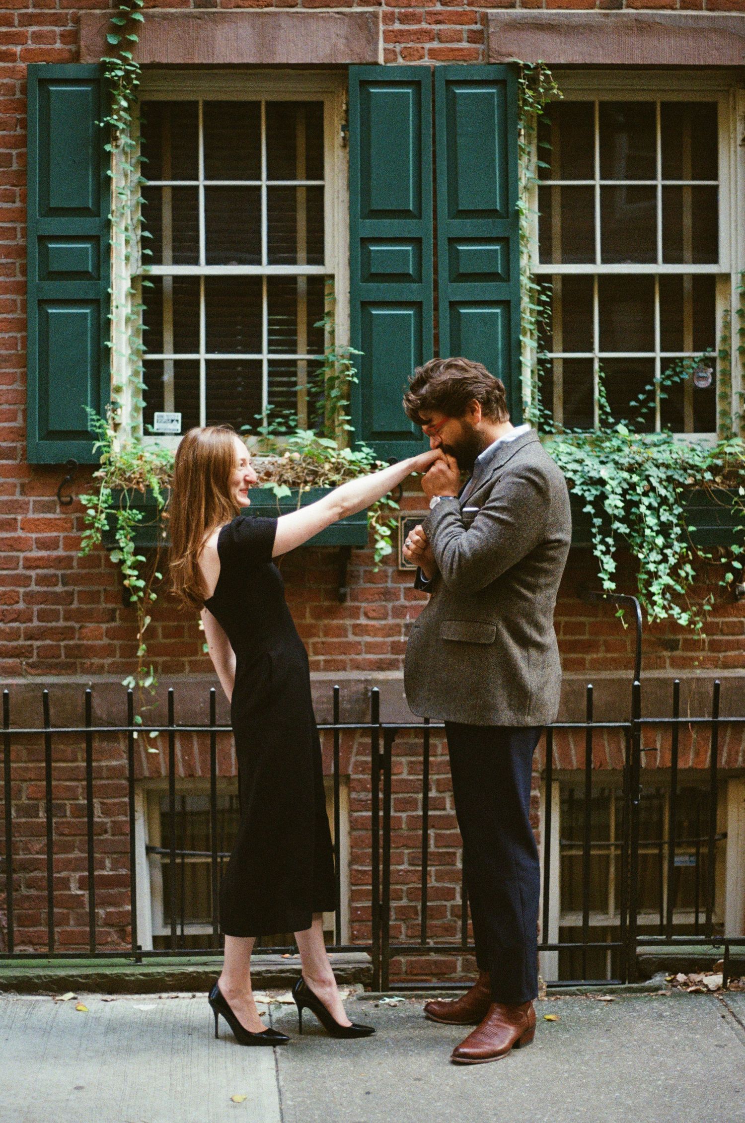 Romantic moment between couple by brick building with green shutters and climbing vines in urban setting.