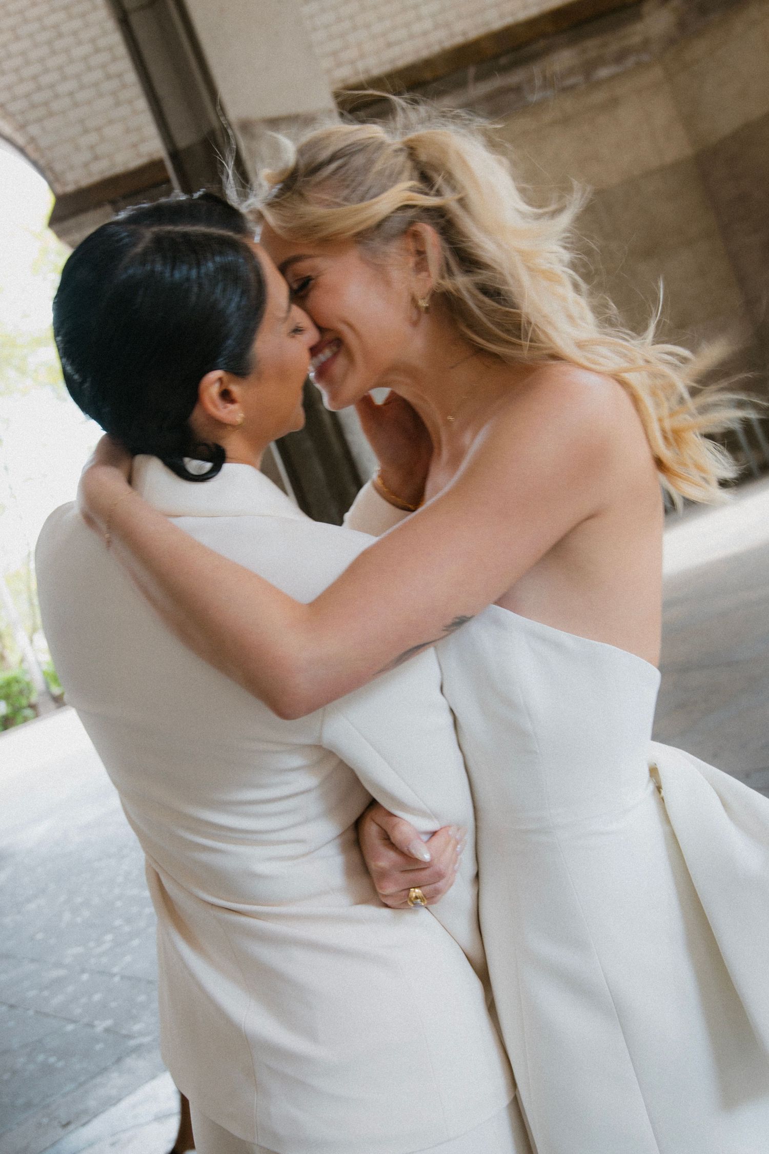 Two people in white outfits share an intimate moment together under an architectural structure.