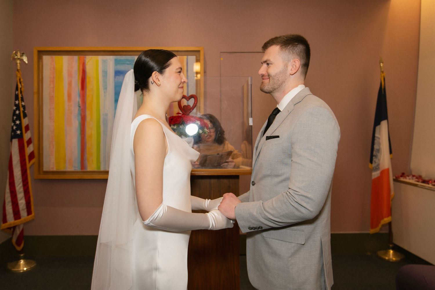 Bride and groom holding hands during intimate city hall wedding ceremony with American and NYC flags in background.