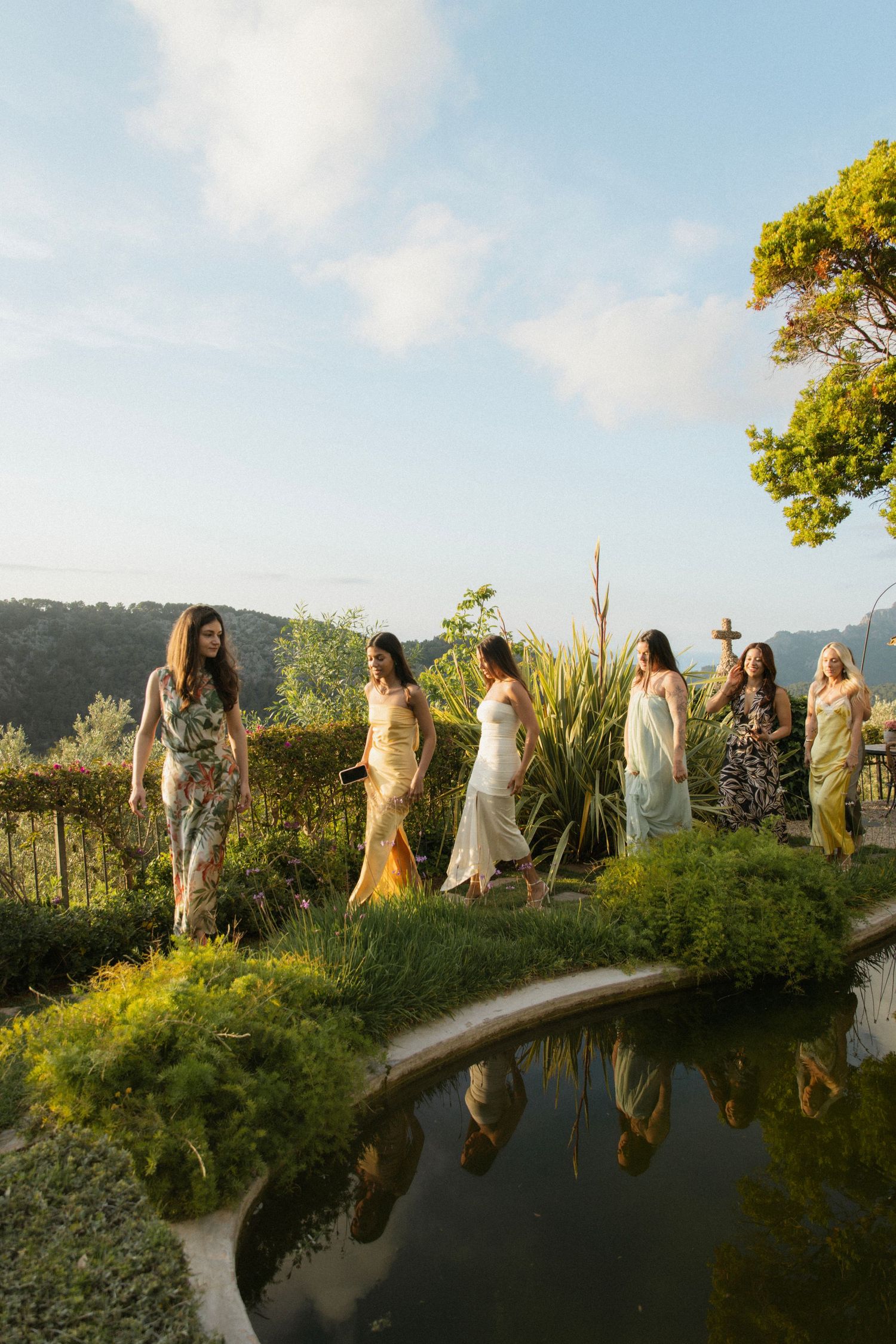 A group of people in light-colored clothing stand together on a curved stone wall during golden hour.