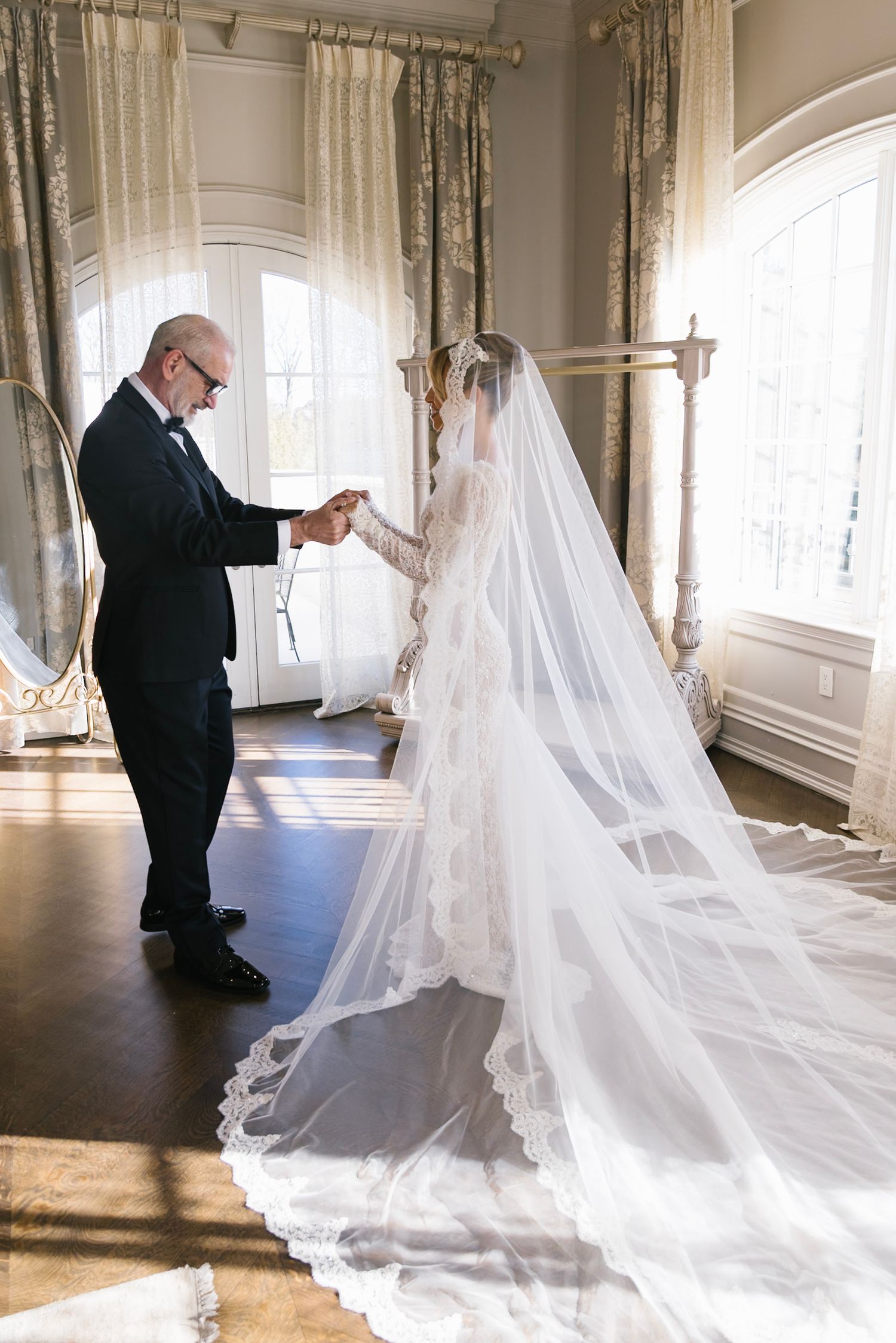A beautiful wedding scene with long flowing veil trailing across a sunlit room as final adjustments are made.
