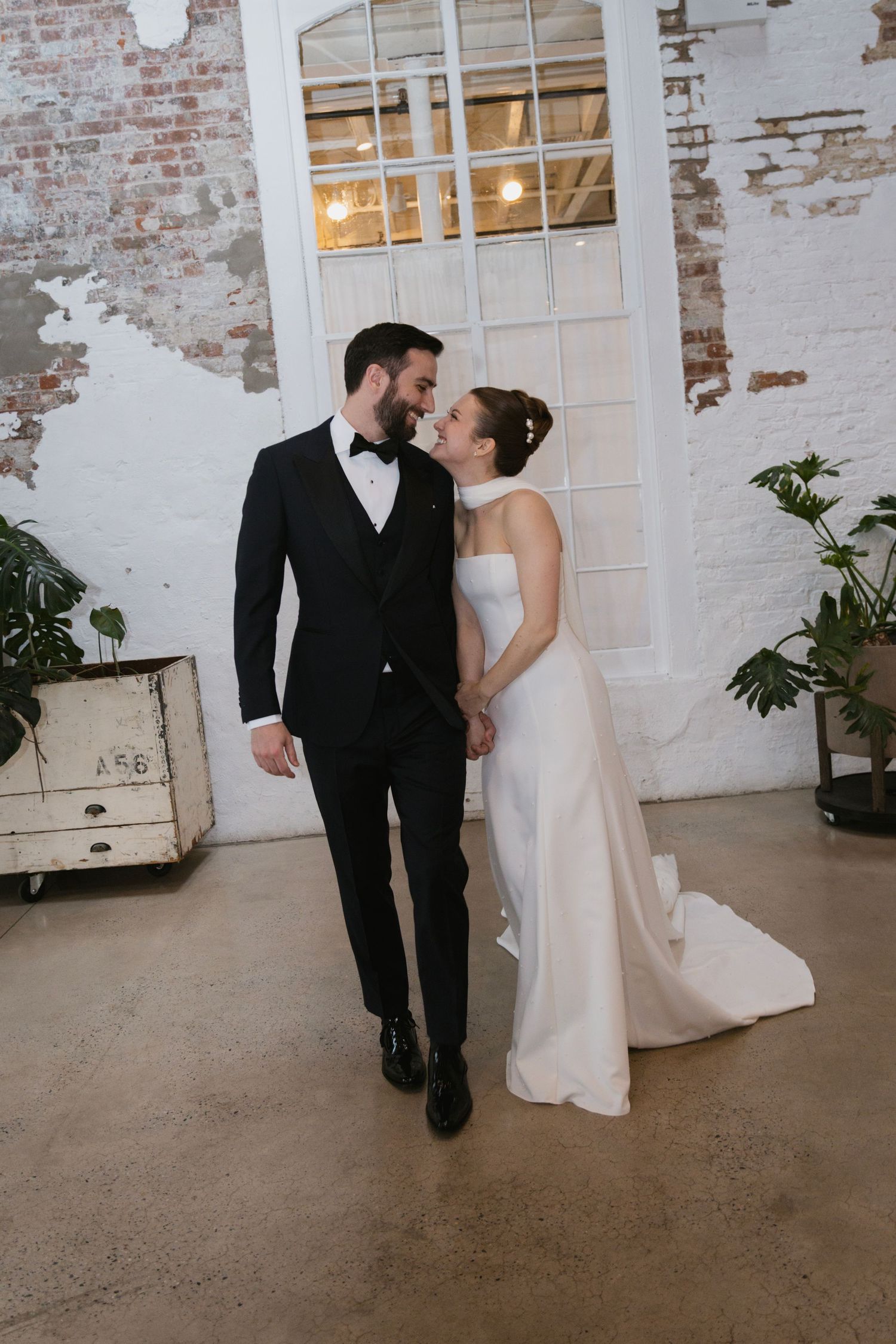 Wedding couple in formal attire sharing intimate moments in industrial chic venue with exposed brick walls.