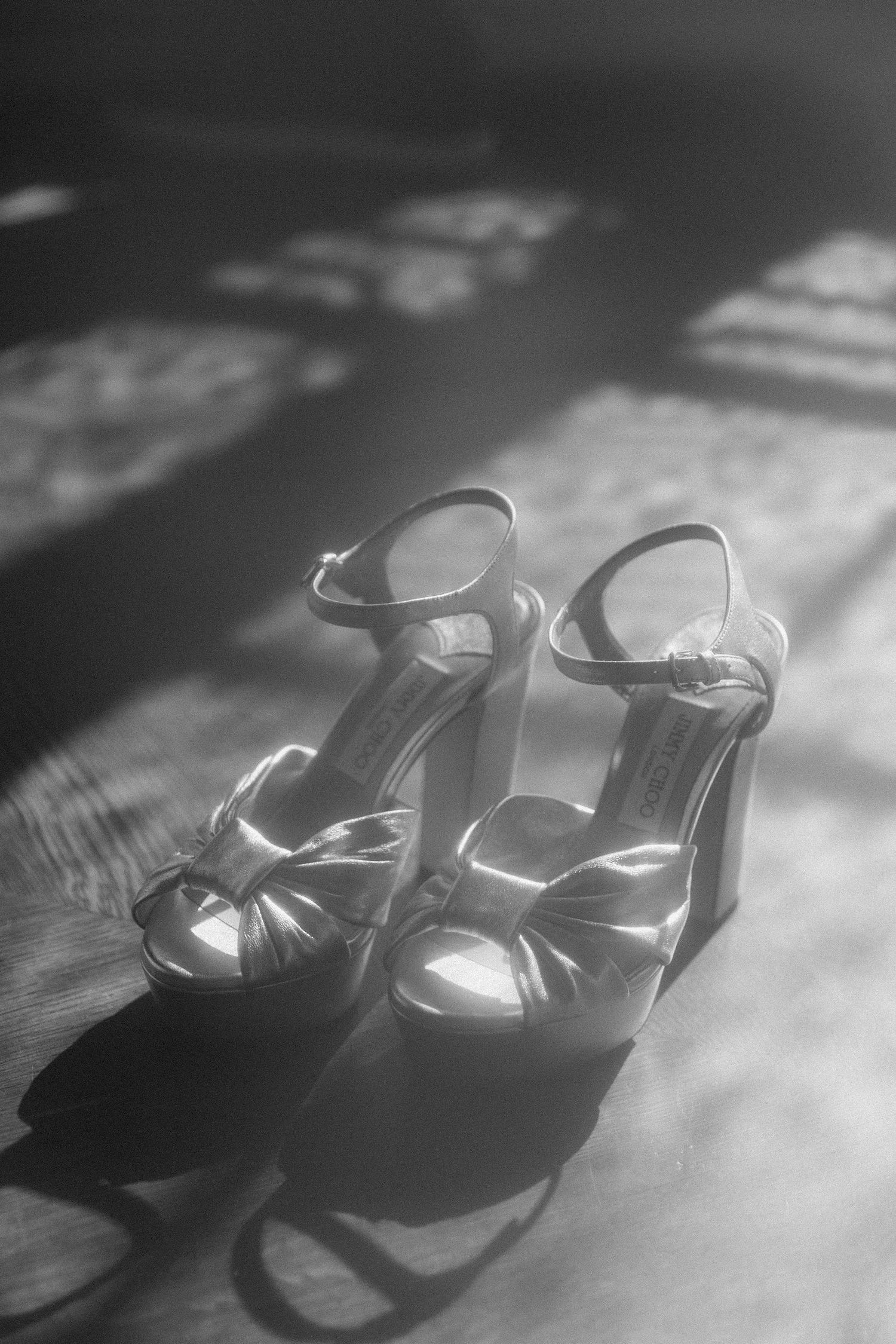 Elegant vintage white bridal heels casting dramatic shadows in black and white photography.