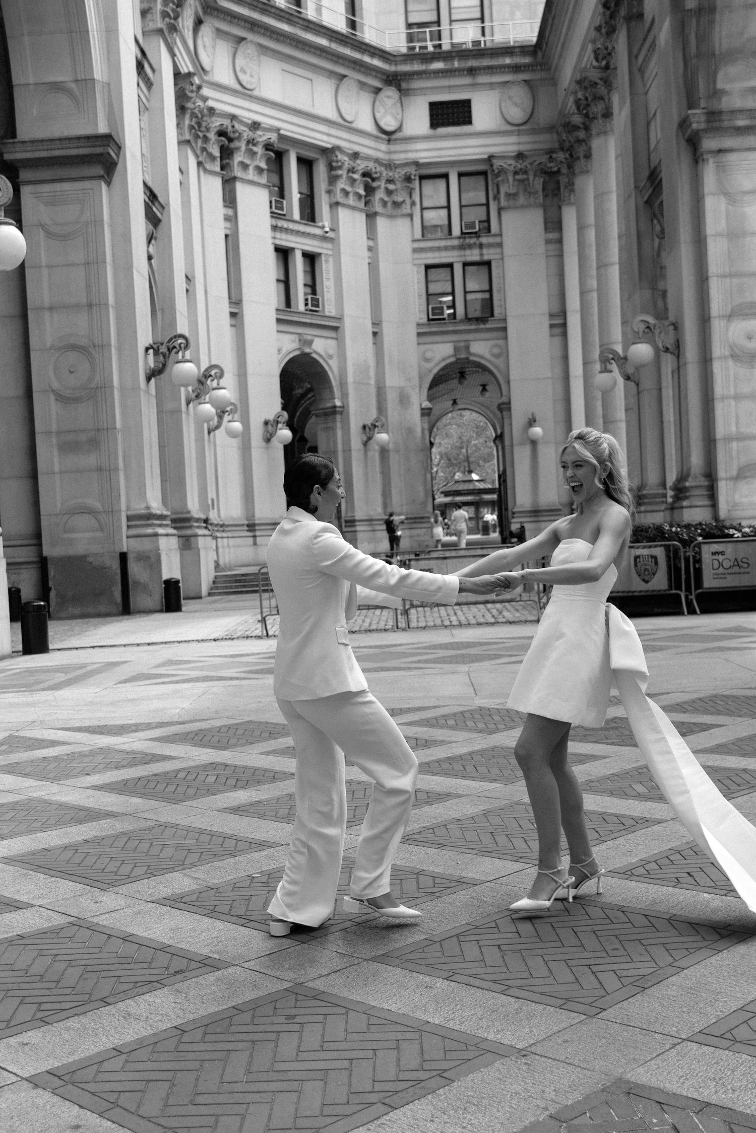 Couple in white outfits dancing gracefully in a grand historic building with ornate architecture and tiled floors.
