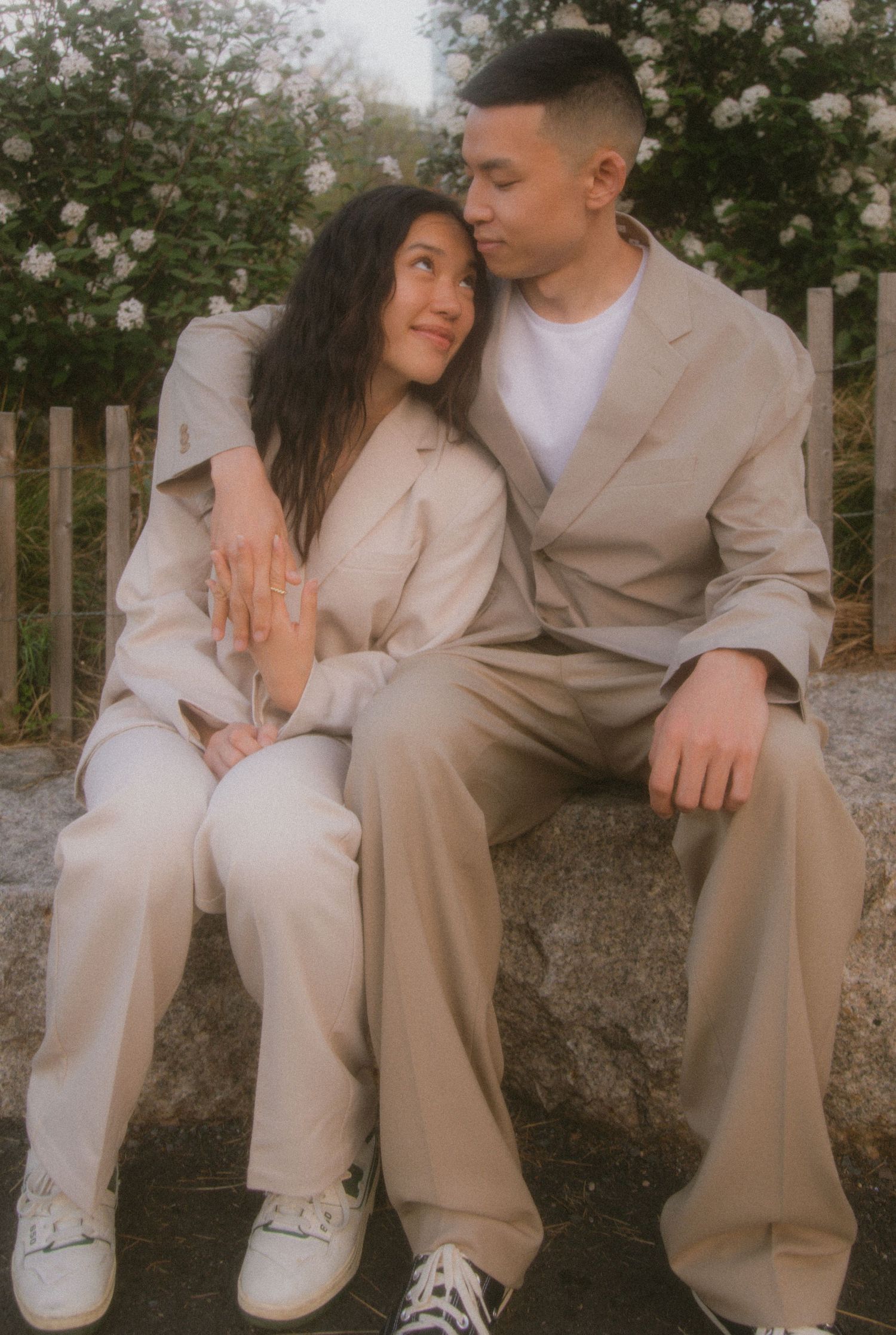 A couple in matching beige outfits sits intimately together, showing multiple romantic poses against an outdoor background.