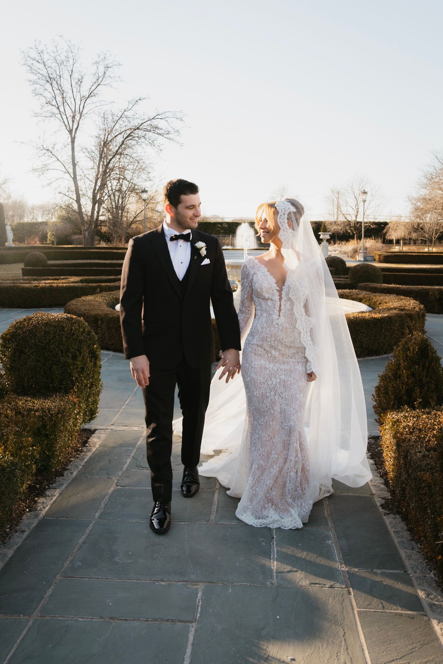 Newlyweds walking together on stone path through manicured garden.