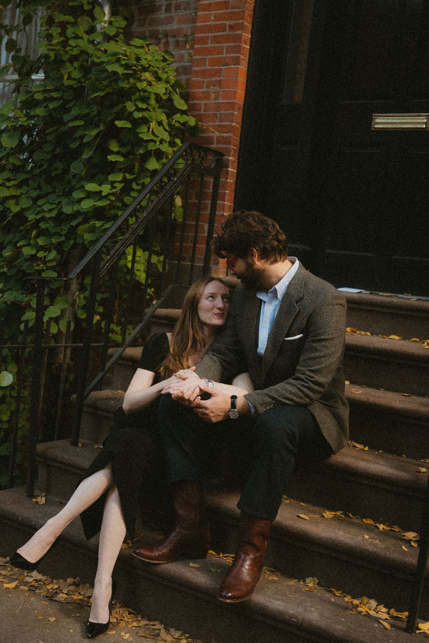 A couple shares a romantic moment on brick steps outside a building with autumn leaves scattered around.