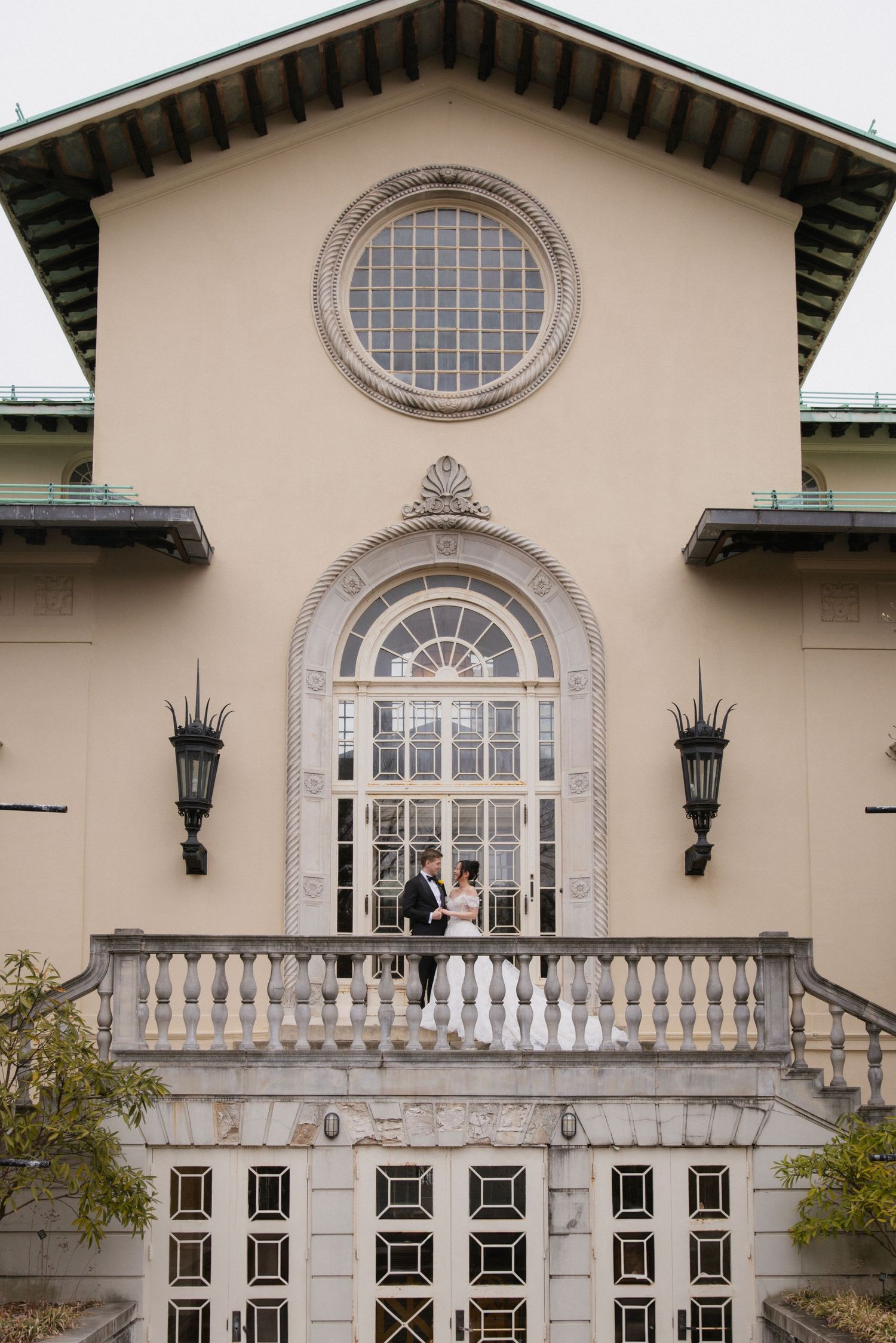 Elegant beige mansion exterior with arched windows, decorative balustrade, and matching wall-mounted lanterns.