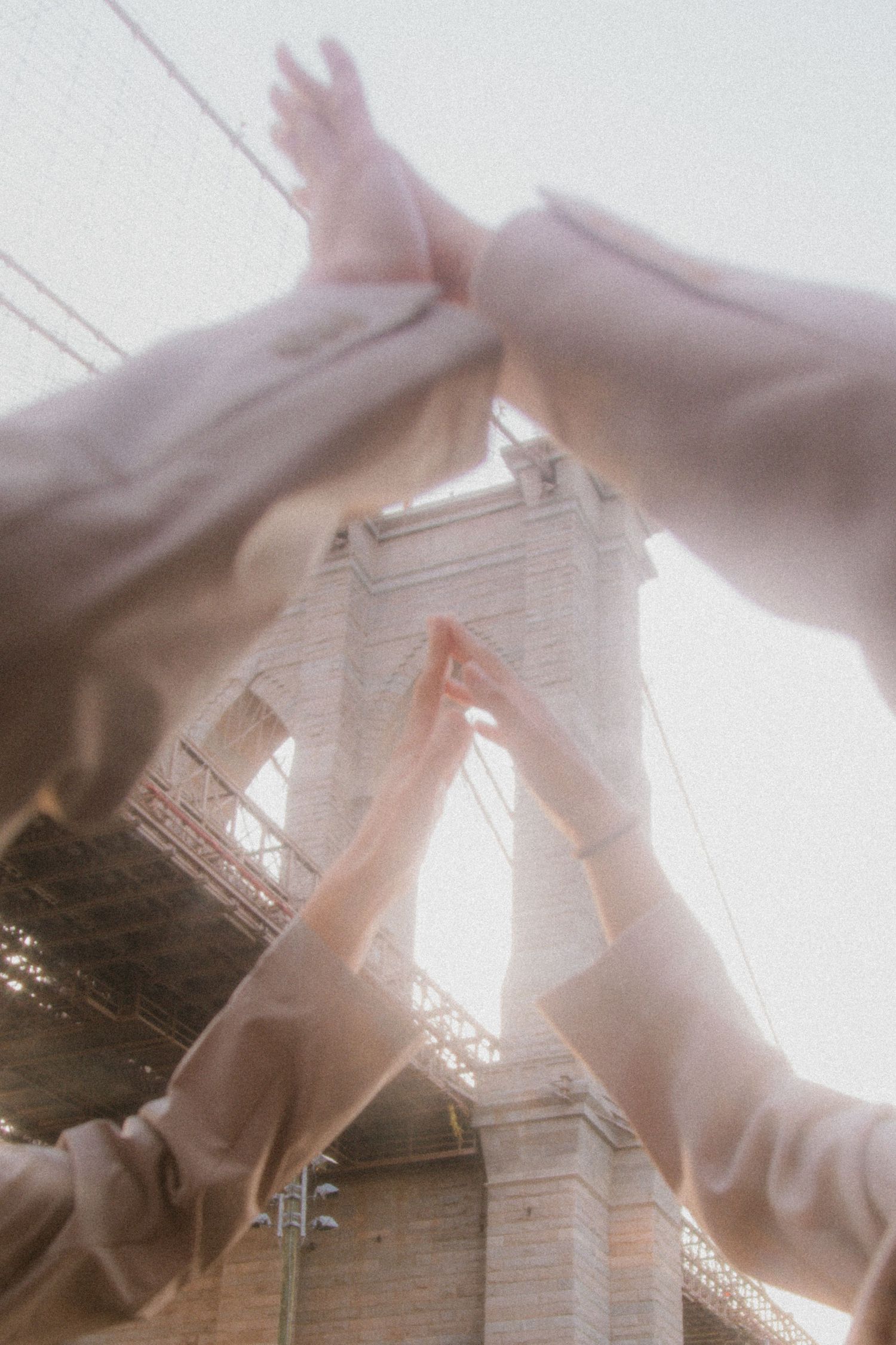 Several hands reaching upward against a bright sky with architectural framing creating a dreamy, ethereal effect.