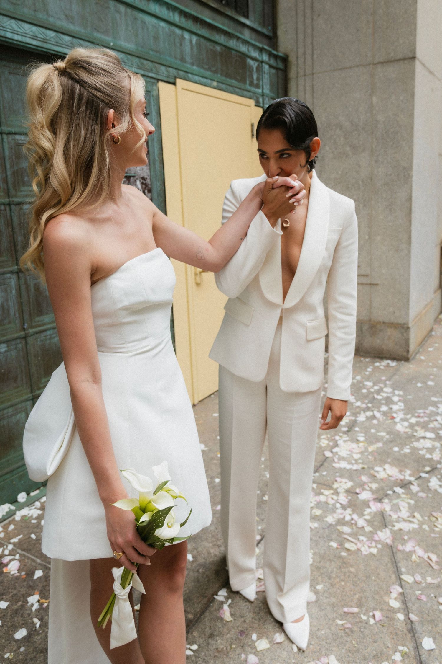 A tender moment between a couple in white wedding attire with scattered petals on the ground.