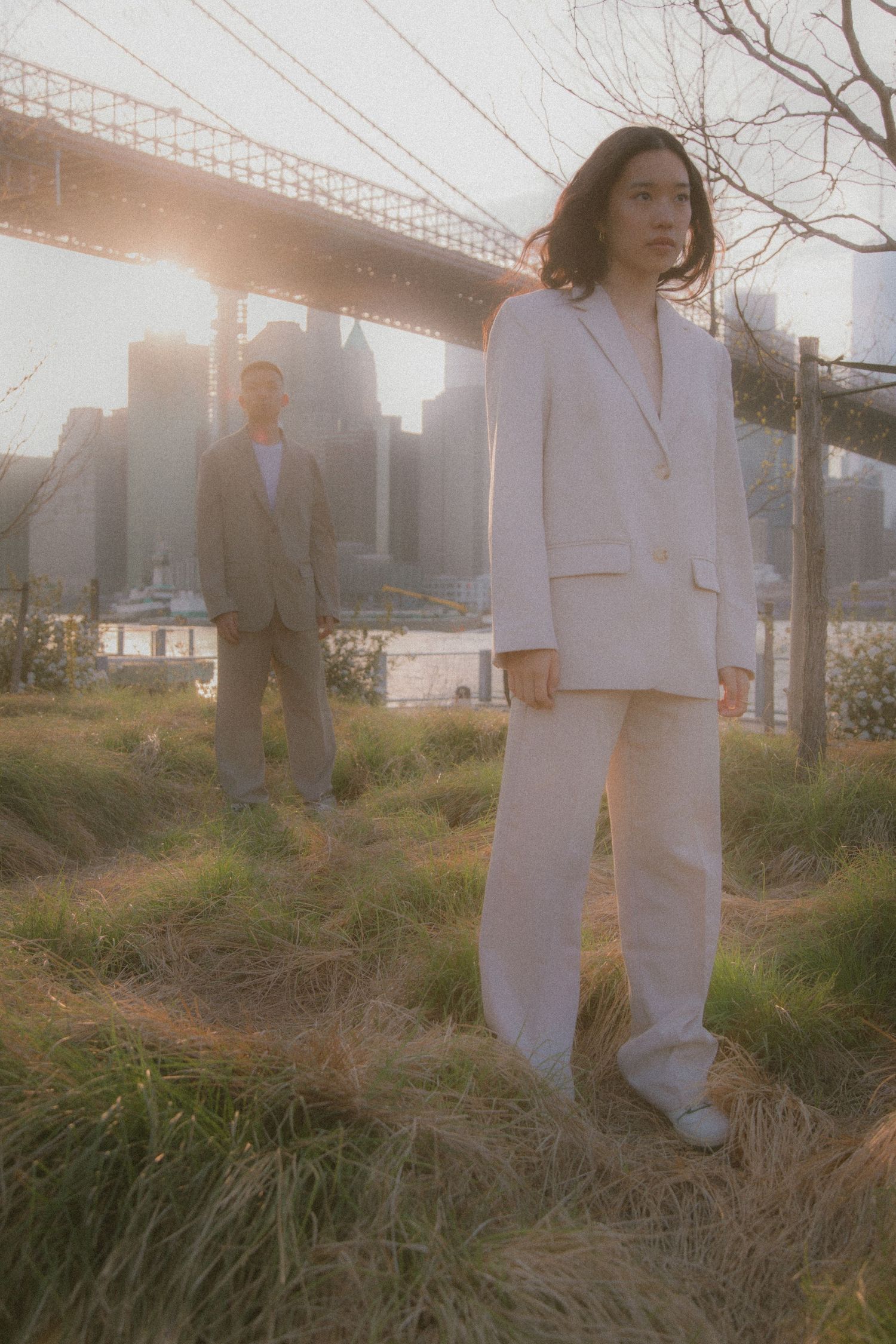 Two people posing against a city skyline with bridge backdrop in dreamy golden hour lighting and tall grass.