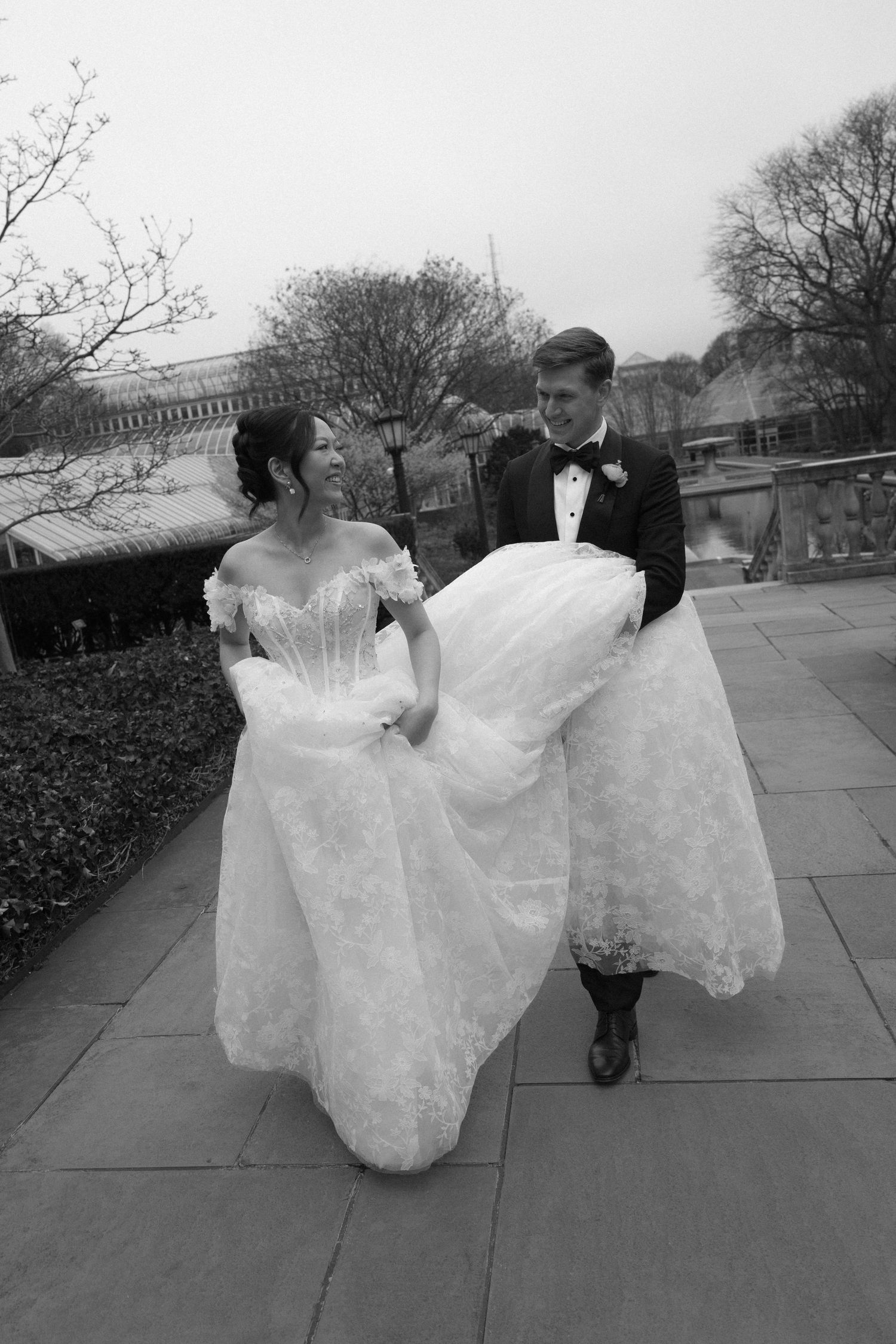 A sequence of black and white photos showing two figures in bridal gowns walking and twirling on an outdoor path.