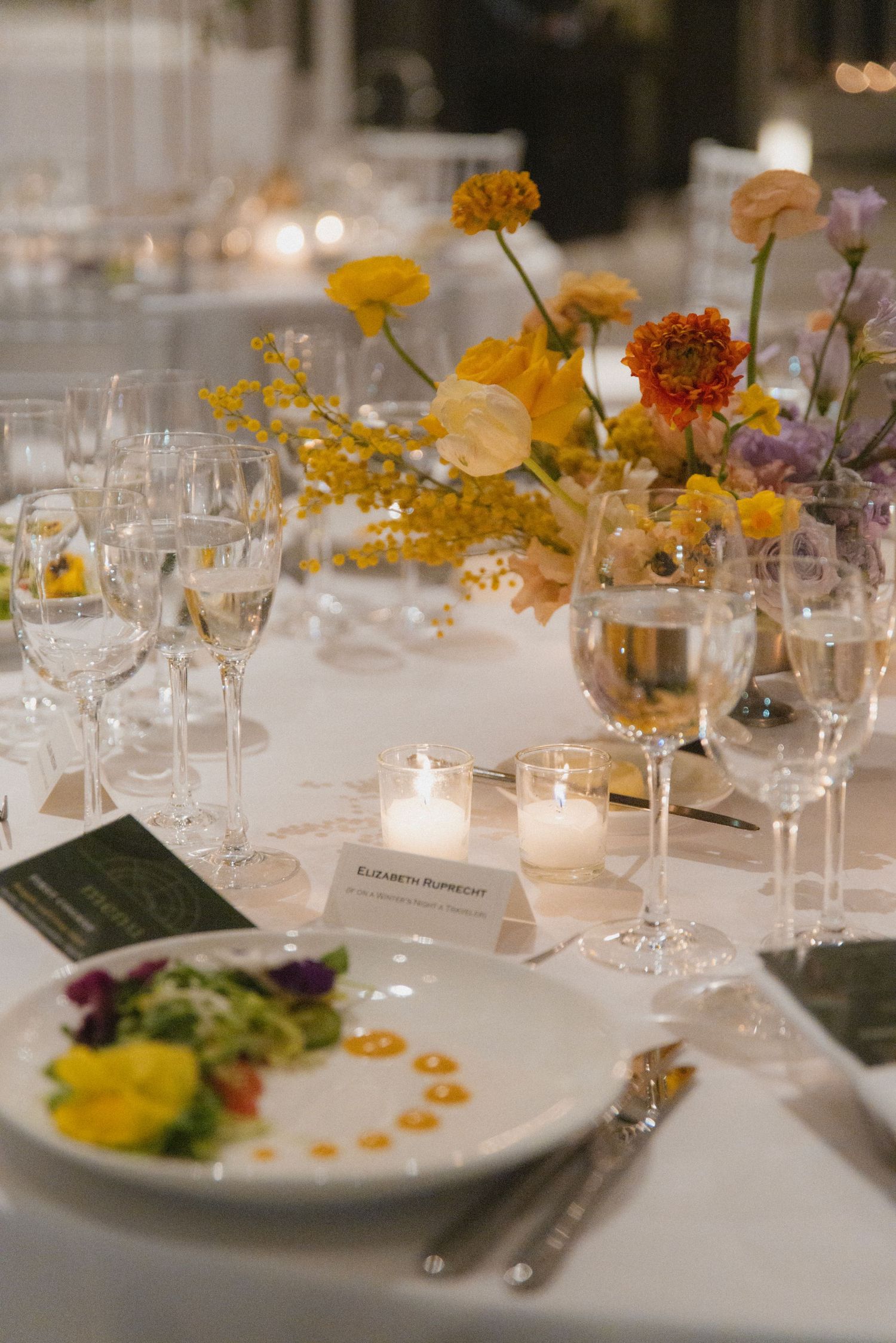 Wedding reception table with yellow floral centerpiece, wine glasses, and elegant place settings.